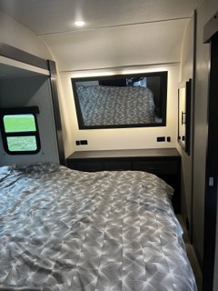 Comfortable RV rental bedroom featuring a bed with patterned bedding, dresser, and illuminated mirror, ready for your next adventure.. Grand Design Momentum 2022