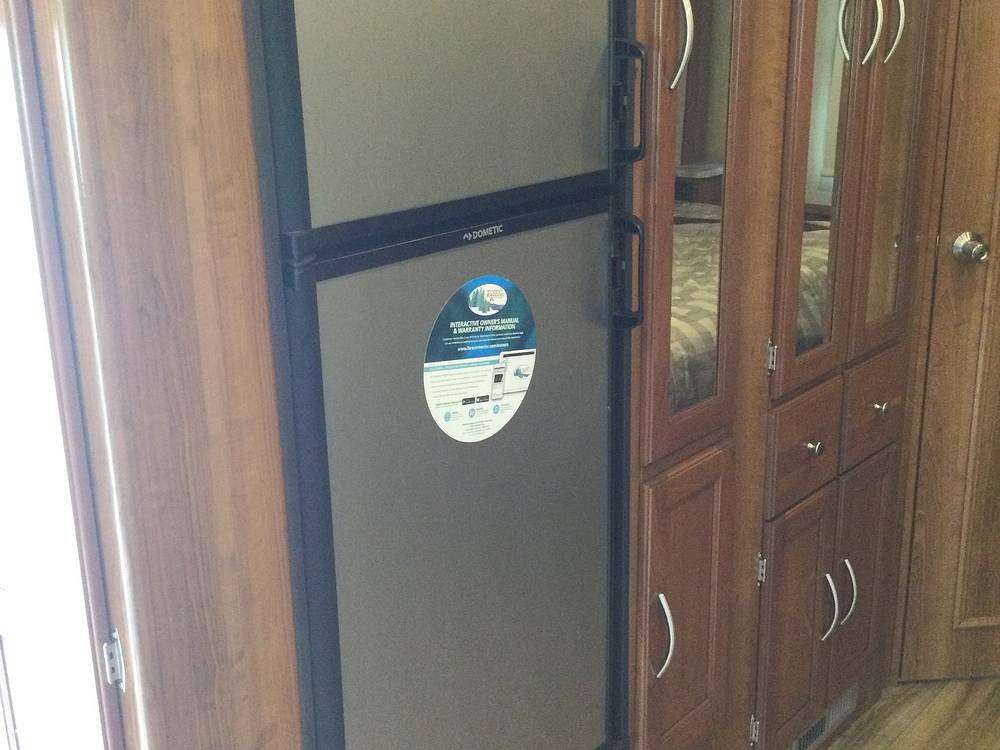 RV rental interior: A Dometic refrigerator next to wooden cabinets with mirrored panels reflecting a bedroom area.. Coachmen Pursuit 27DS 2019