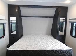 Comfortable RV rental bedroom featuring a queen bed, integrated headboard/storage, and side windows, ideal for travel.. Coachmen Freedom Express 2023