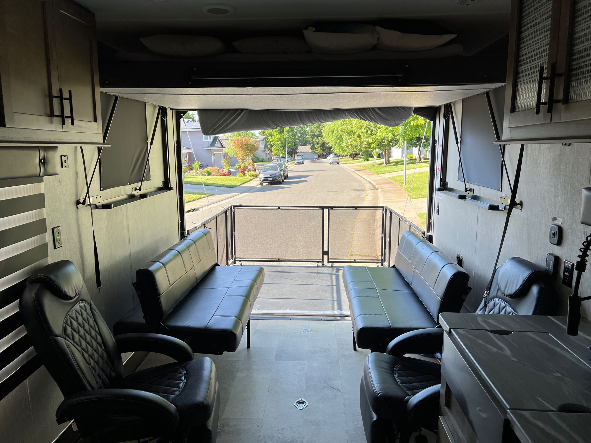 RV rental ready for adventure: Inside a toy hauler, showing seating, bed loft, and the rear ramp open to a neighborhood street.. Rogue Vengeance 2021