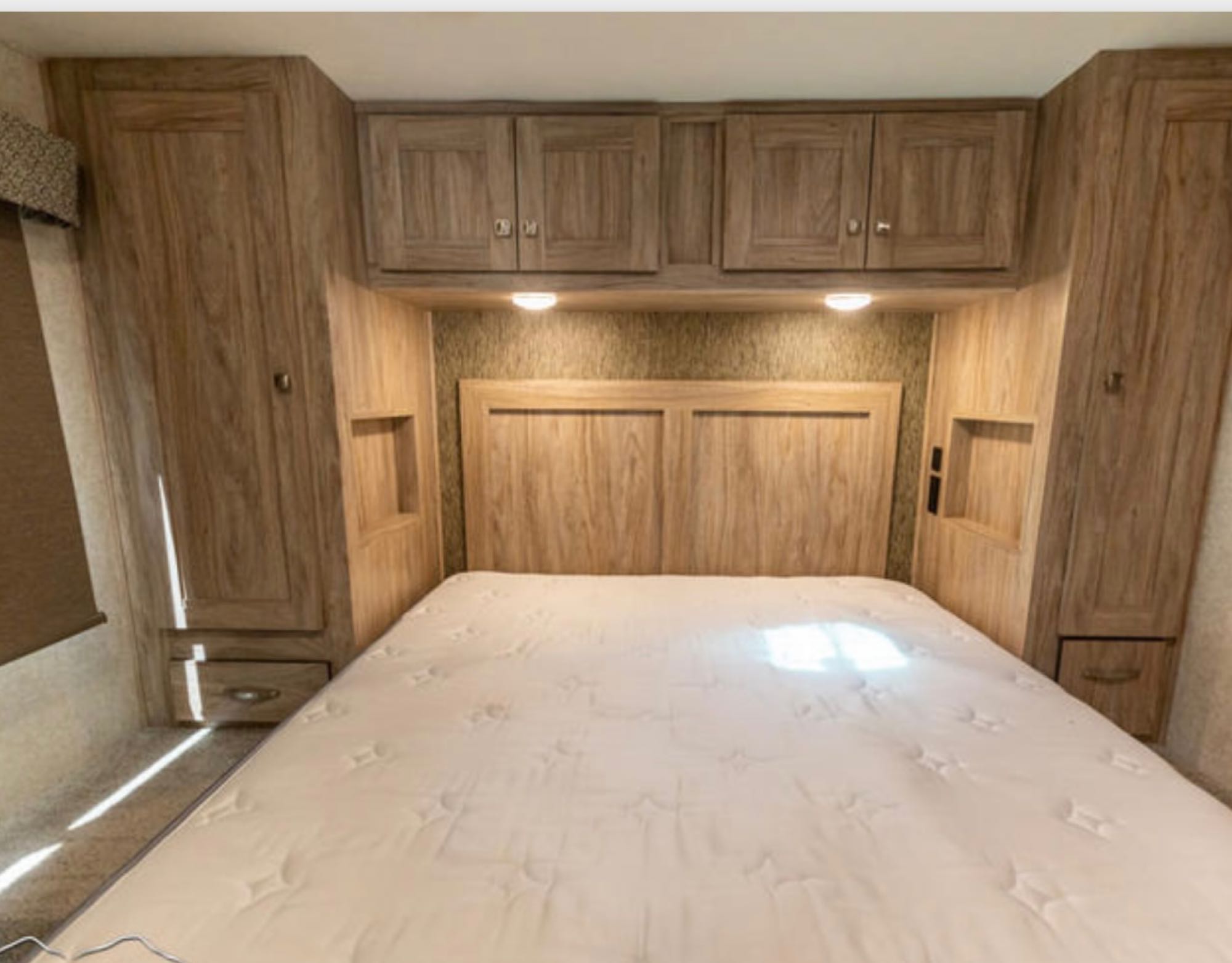 This inviting RV rental bedroom features a comfy bed, integrated storage, overhead cabinets, and soft lighting for a relaxing stay.. Forest River Sun Seeker 2020