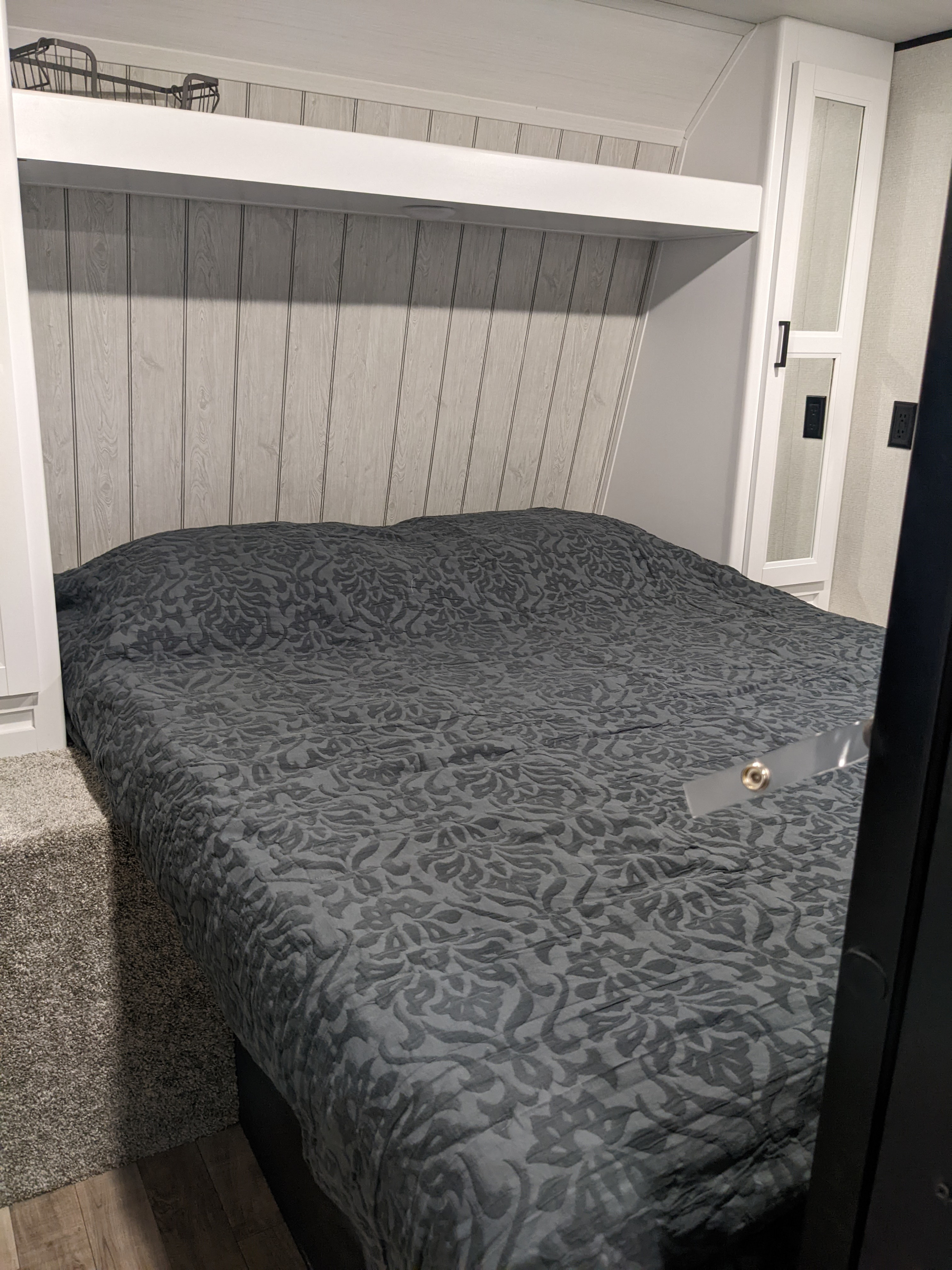 Cozy RV rental bedroom featuring a patterned dark gray bed, light wood-look paneling, and ample storage.. Keystone RV Hideout 2022