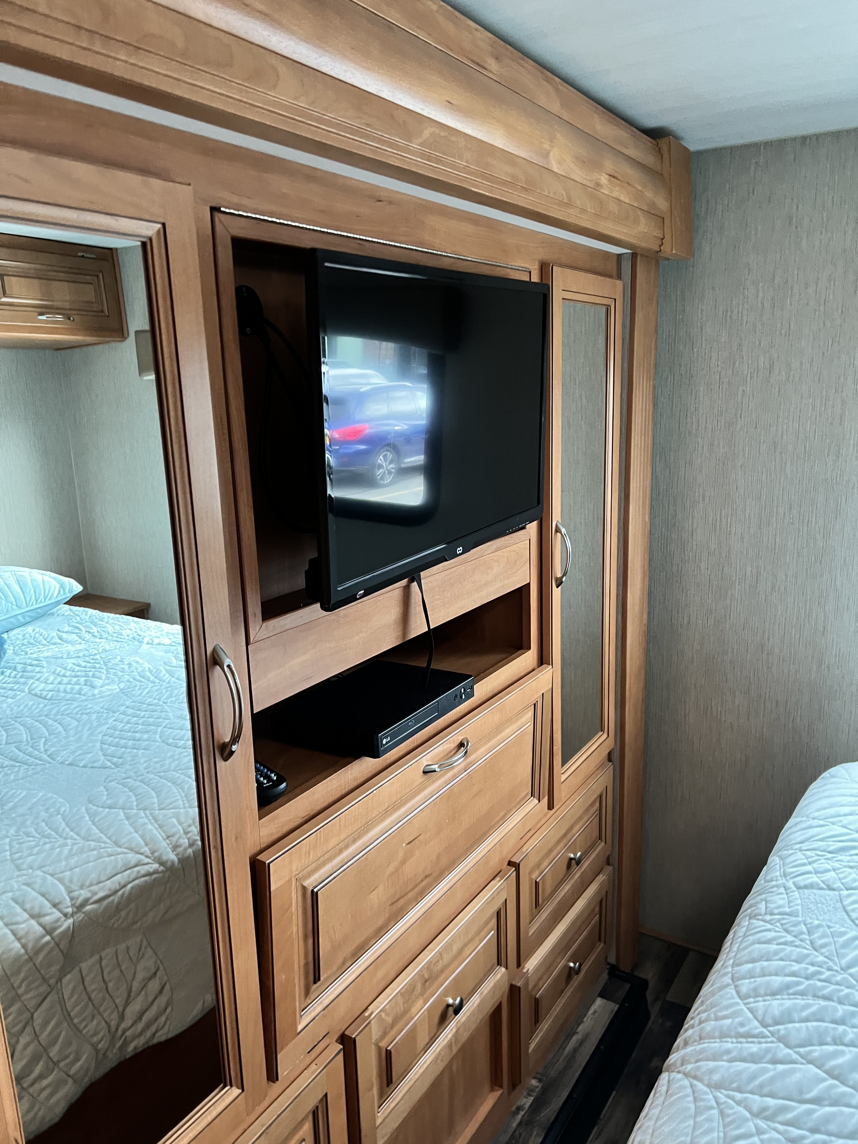 RV rental bedroom: a sleek wood entertainment center with a TV, Blu-ray player, and ample storage. Mirrored doors reflect the comfy bed.. Nexus Phantom 32P 2019