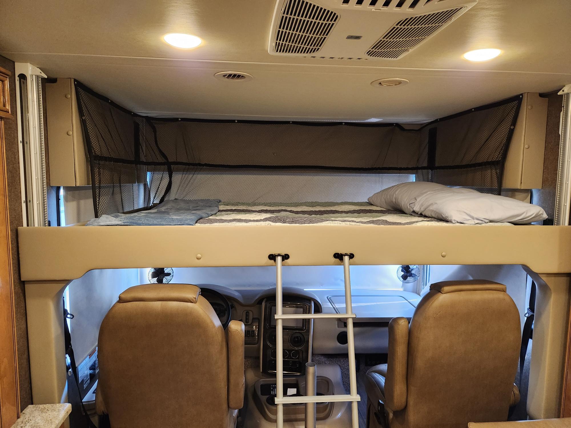 RV rental interior: a cozy cab-over bunk with a safety net & ladder, above the cockpit seats and dashboard.. Thor Challenger 2019