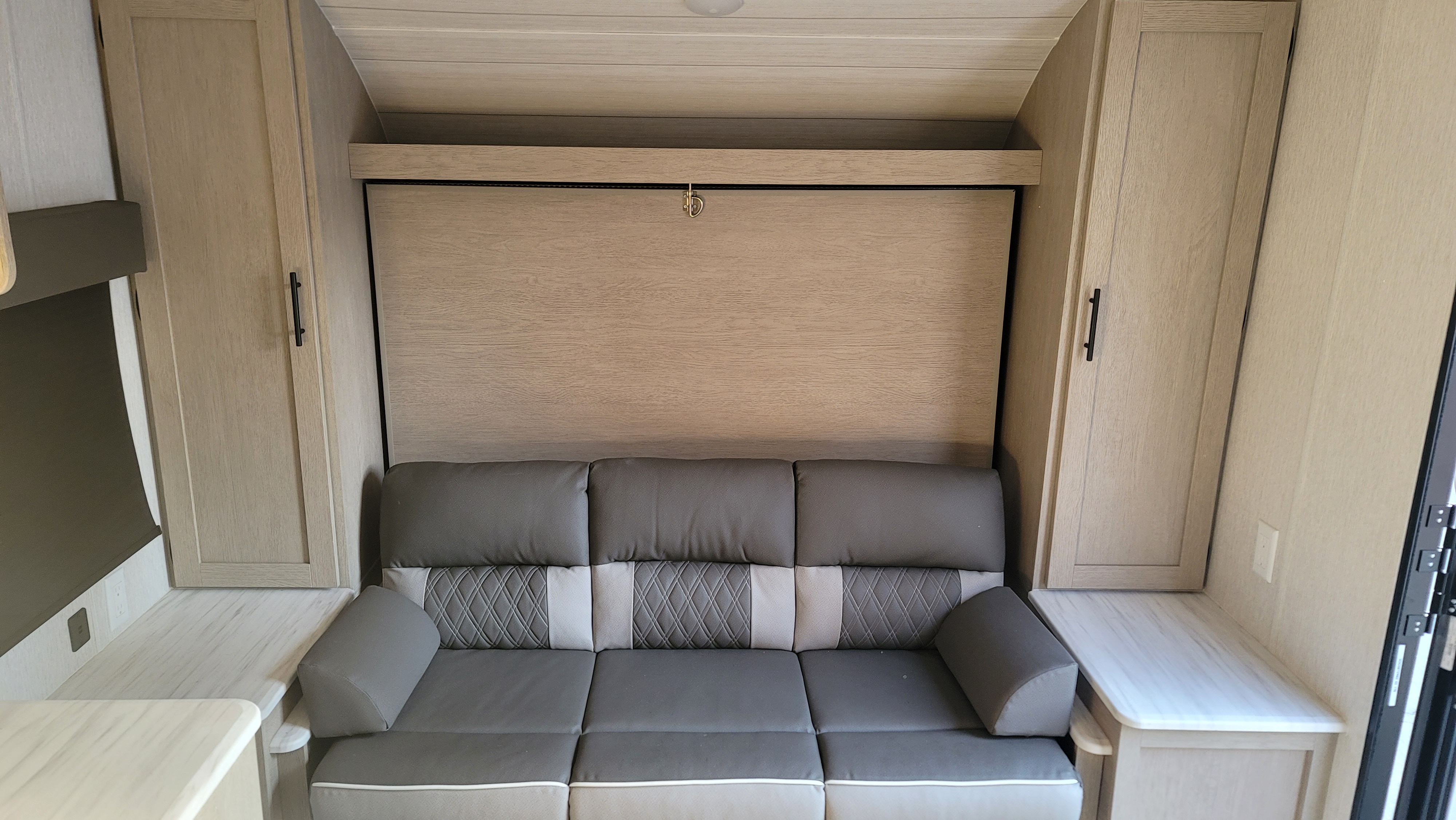 Modern RV rental living area featuring a comfortable sofa and a space-saving murphy bed system with built-in side cabinets and counter space.. Forest River Forest River EVO 2023