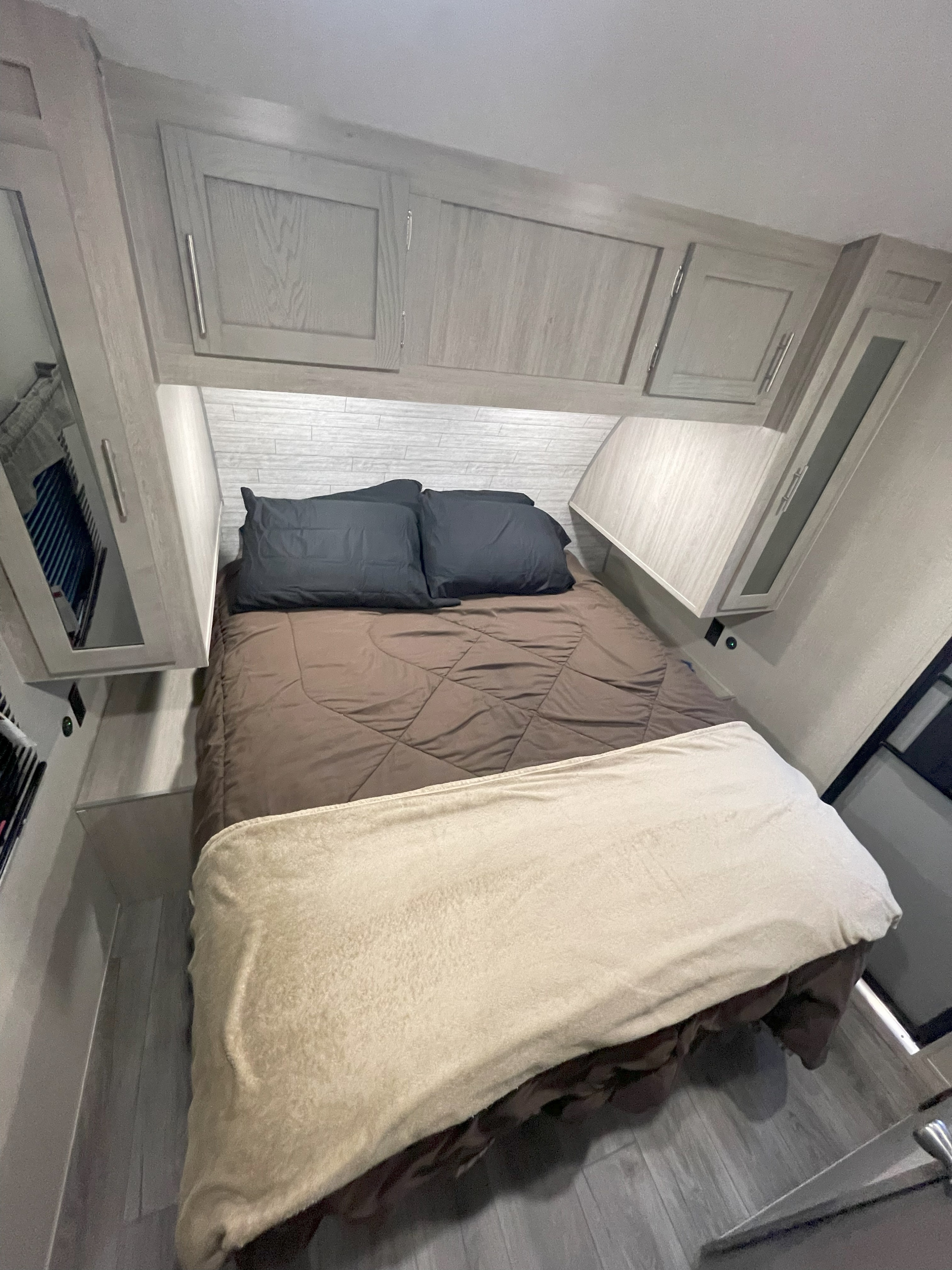 Cozy RV rental bedroom interior with light wood cabinets, bed, and textured wall, offering compact comfort.. Coachmen Catalina 2023