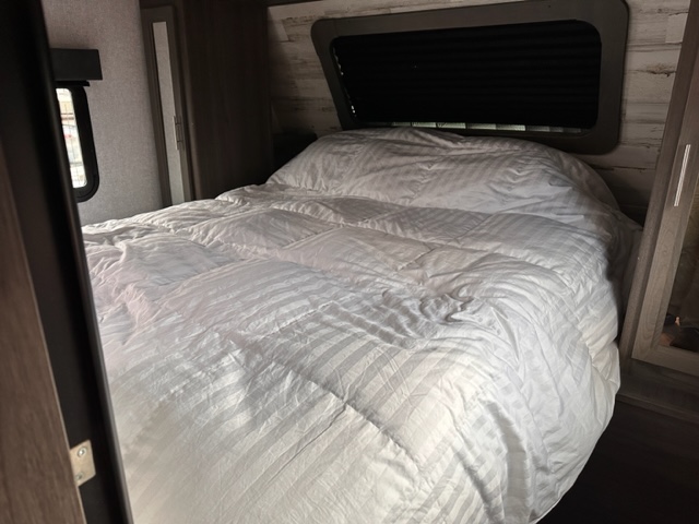 Inviting RV rental bedroom with a large bed, featuring fluffy white, striped bedding and two windows.. Dutchmen Kodiak Ultimate 2021