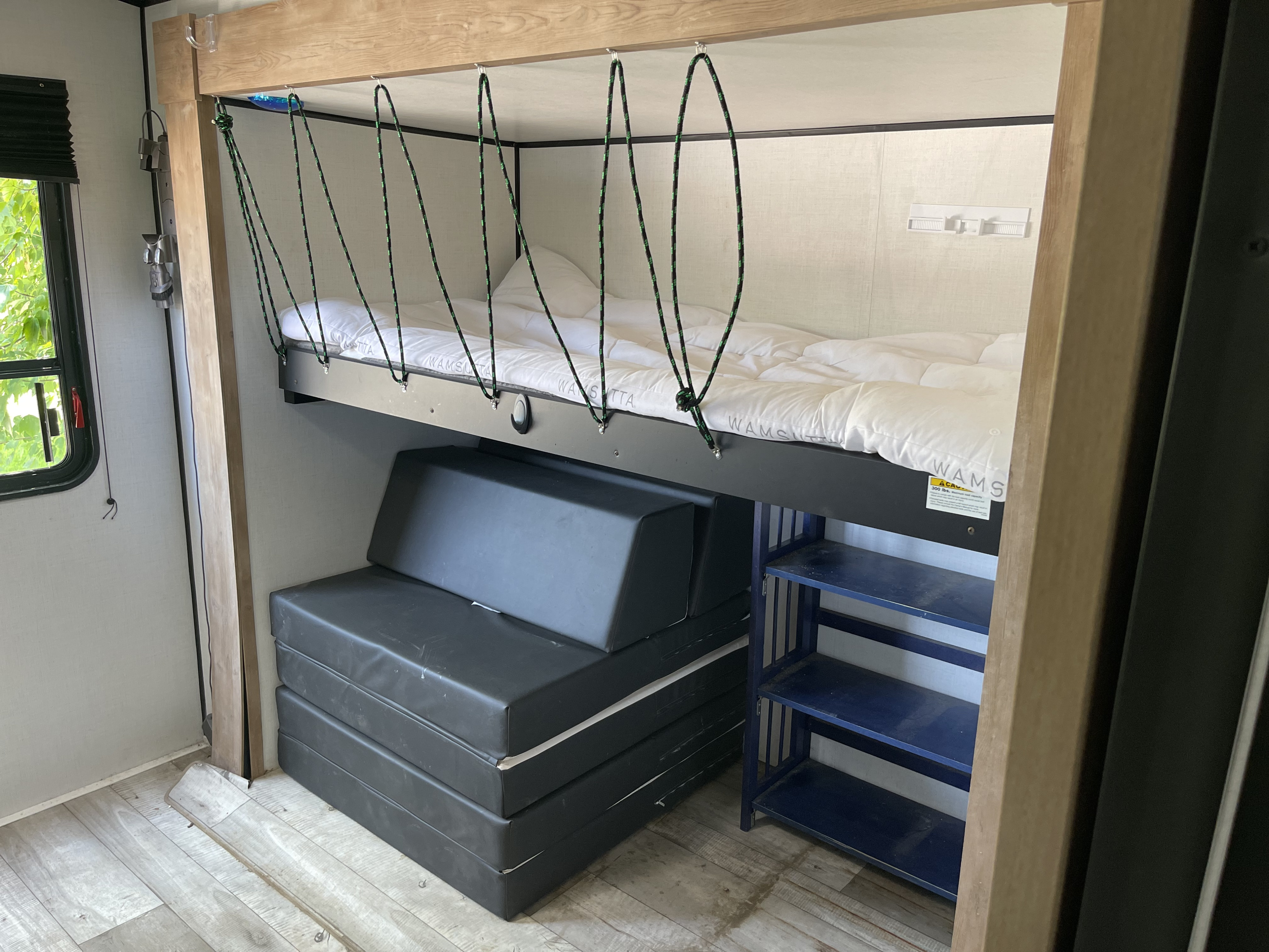 This RV rental features a bunk bed with safety ropes above a convertible sofa and shelves, optimizing compact living.. Keystone RV Springdale 2023