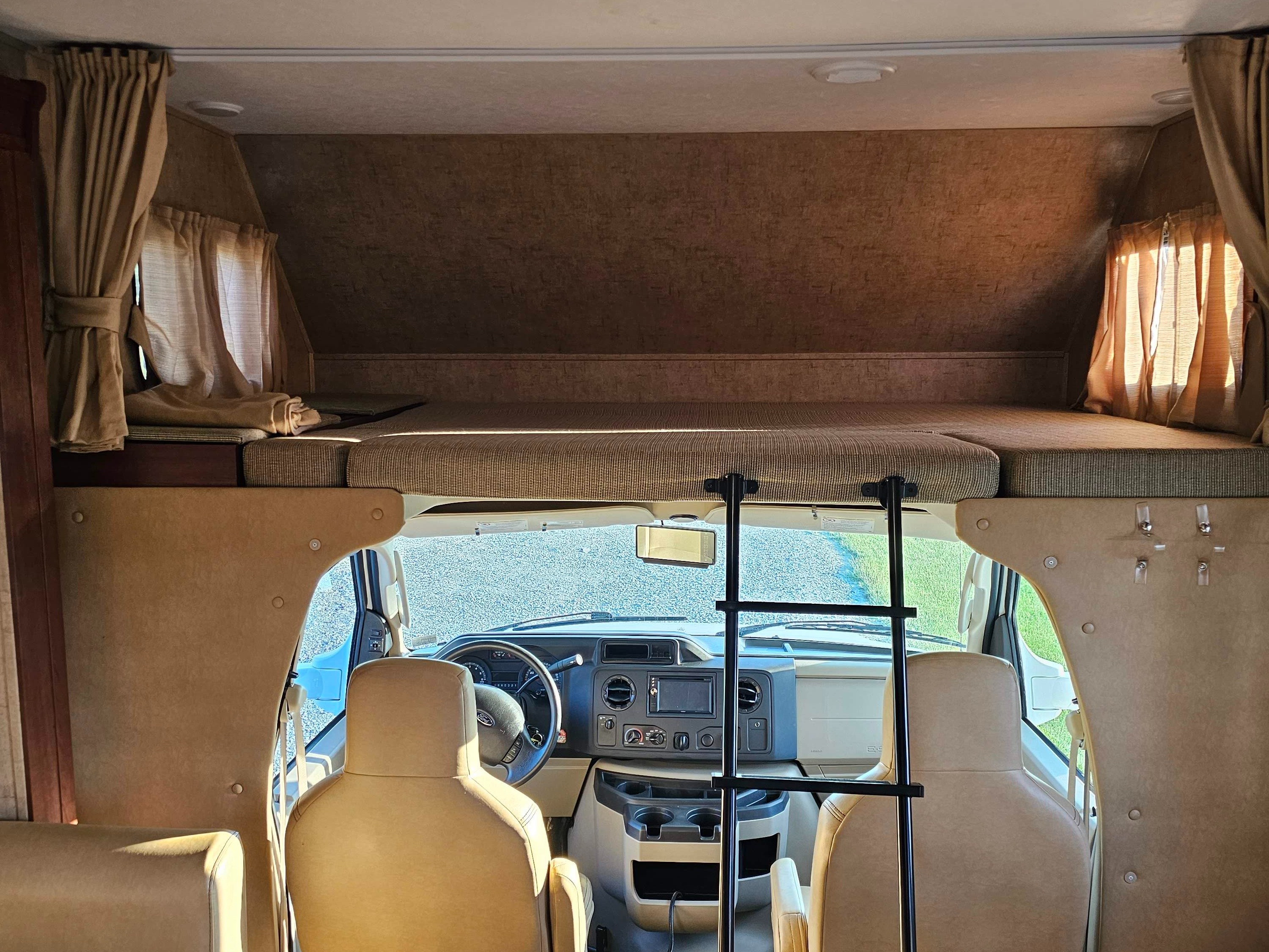 Spacious RV rental interior featuring an overhead bunk bed with ladder, and the vehicle's front cockpit.. Forest River Sunseeker 2015