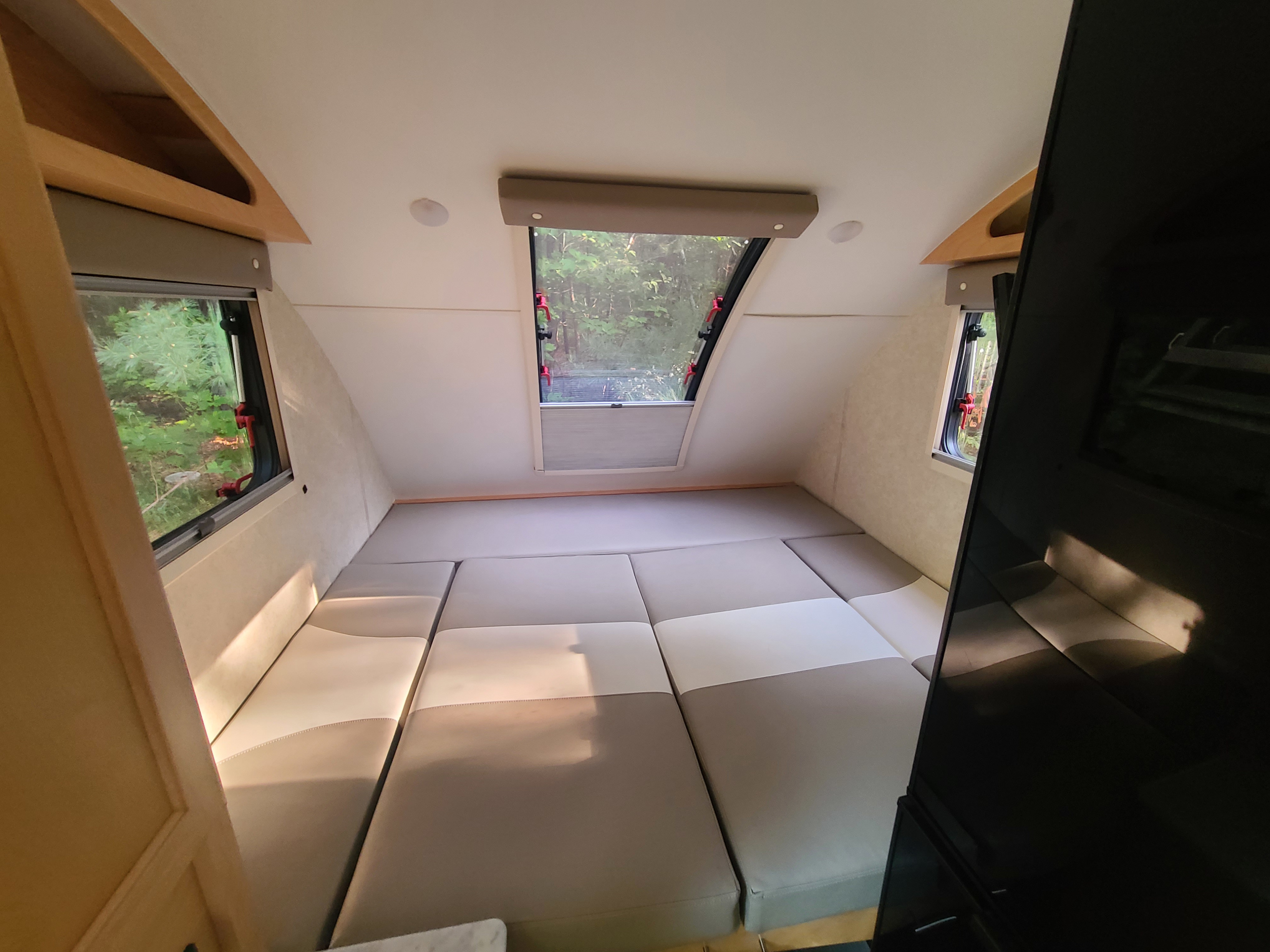 Spacious rv rental interior with convertible bed/seating area, light & dark cushions, and panoramic forest views from large windows.. Xtreme Outdoors Little Guy 2019