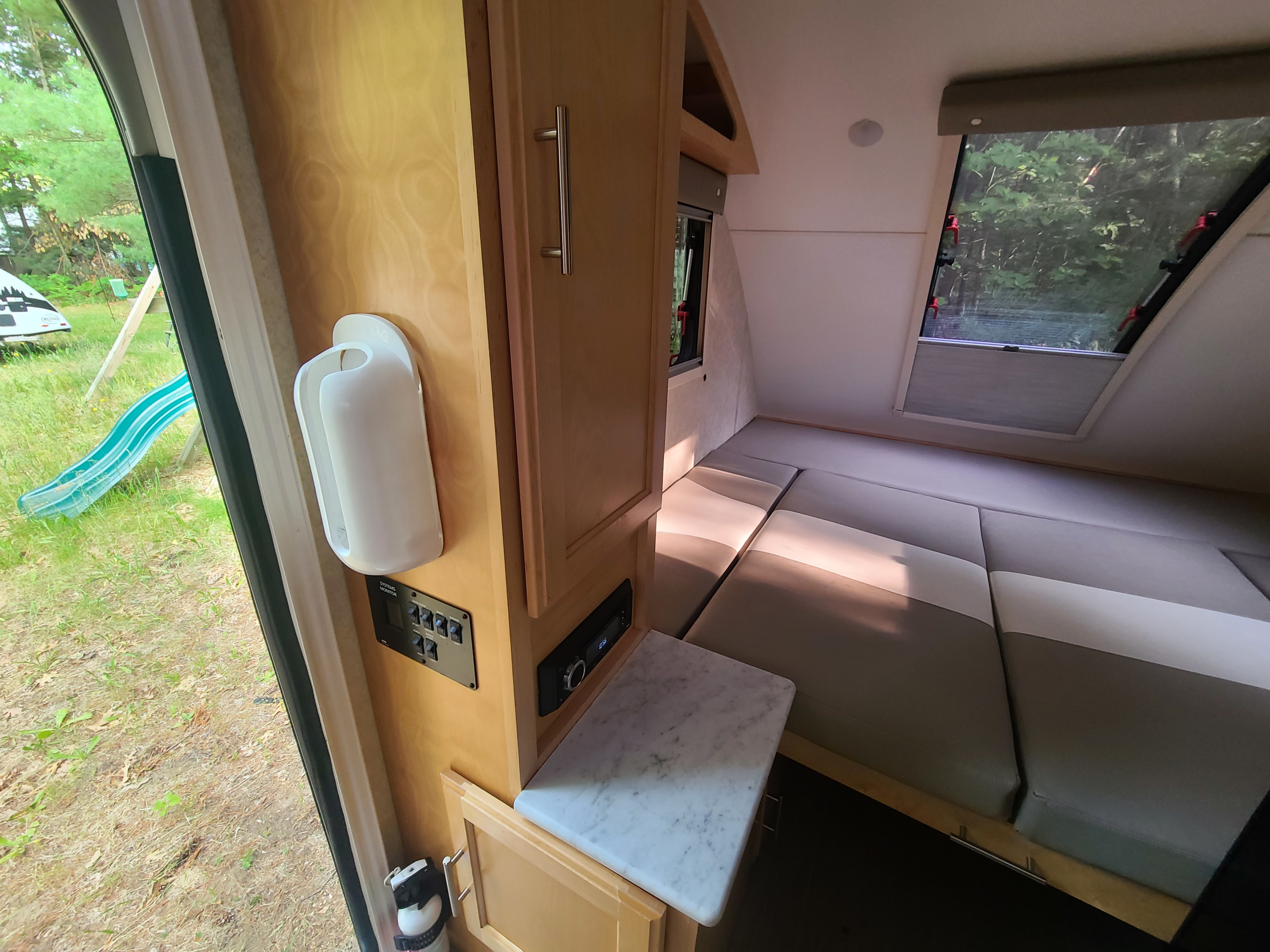 Inside an RV rental: Compact living space with convertible bed, system controls, and outdoor view through the door.. Xtreme Outdoors Little Guy 2019