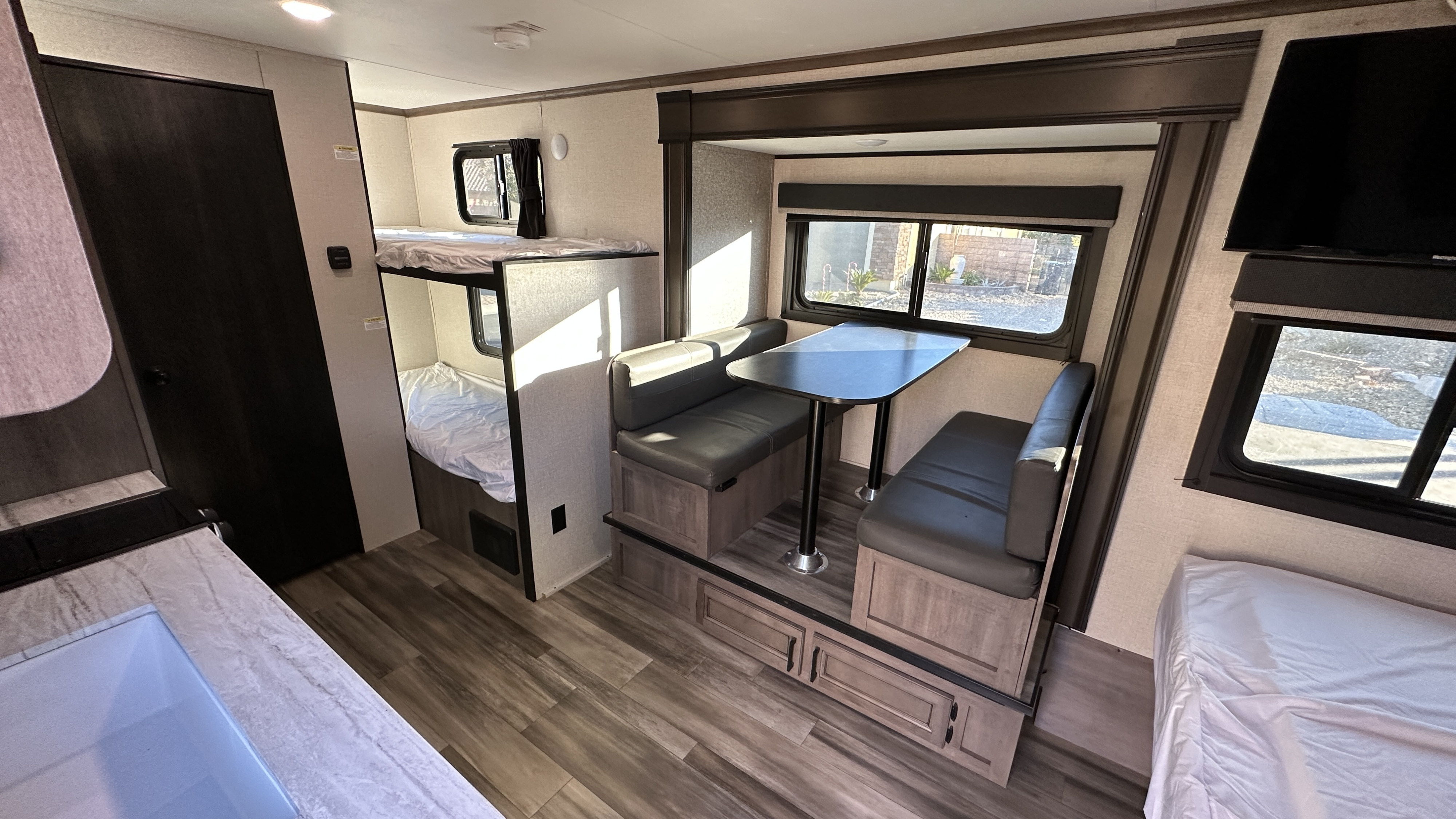 Inside this RV rental: a bunk bed area, a dinette with dark seating, and a kitchen counter, all with wood-look flooring.. Starcraft Autumn Ridge 2022