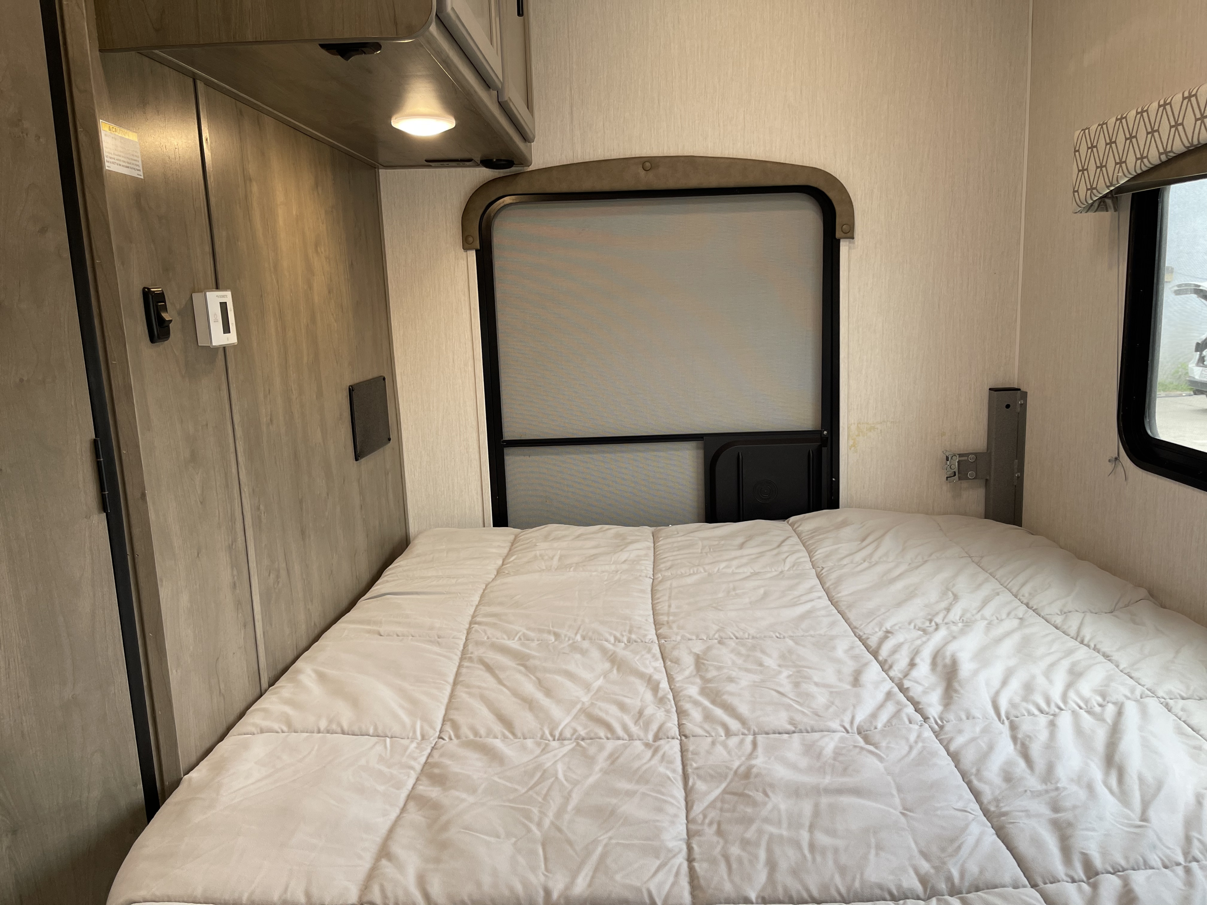 RV rental interior: A cozy bedroom with a white comforter, large screened window, and wall controls.. Coachmen Freelander 2021