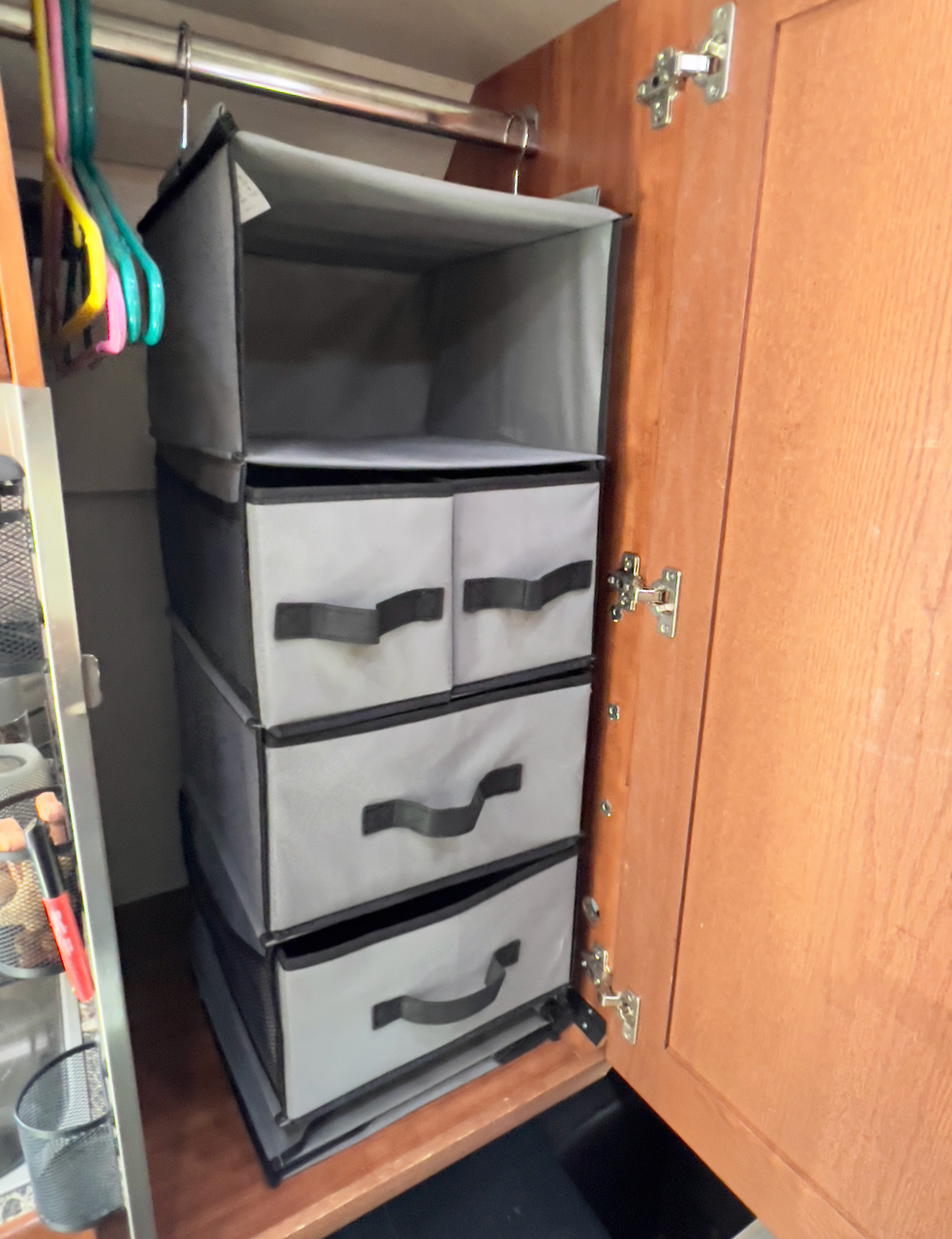 RV rental closet storage: A multi-tiered gray fabric organizer with pull-out drawers hangs from a rod in a wooden wardrobe.. Roadtrek Simplicity SRT 2019