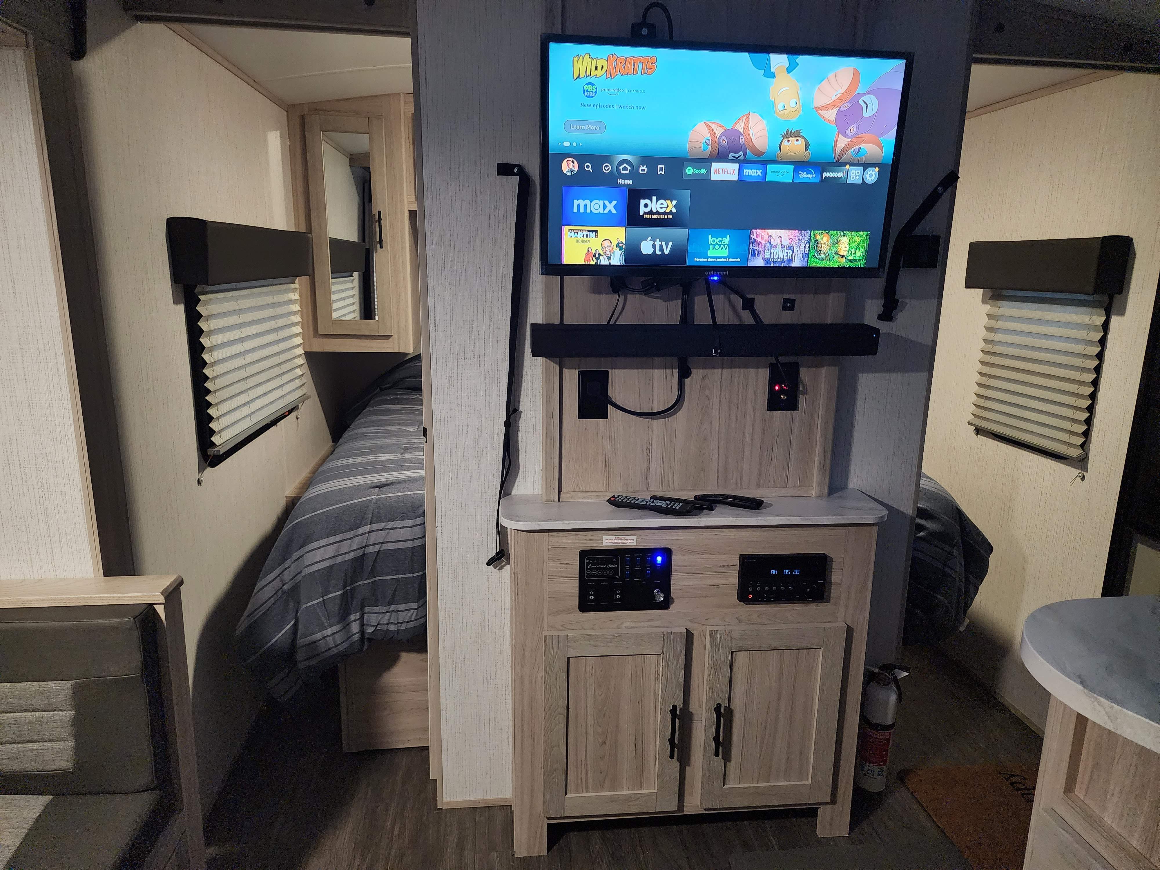 RV rental with a smart TV displaying streaming apps for family entertainment, plus a cozy bedroom area and control panel.. Heartland RVs Shadow Cruiser 2023