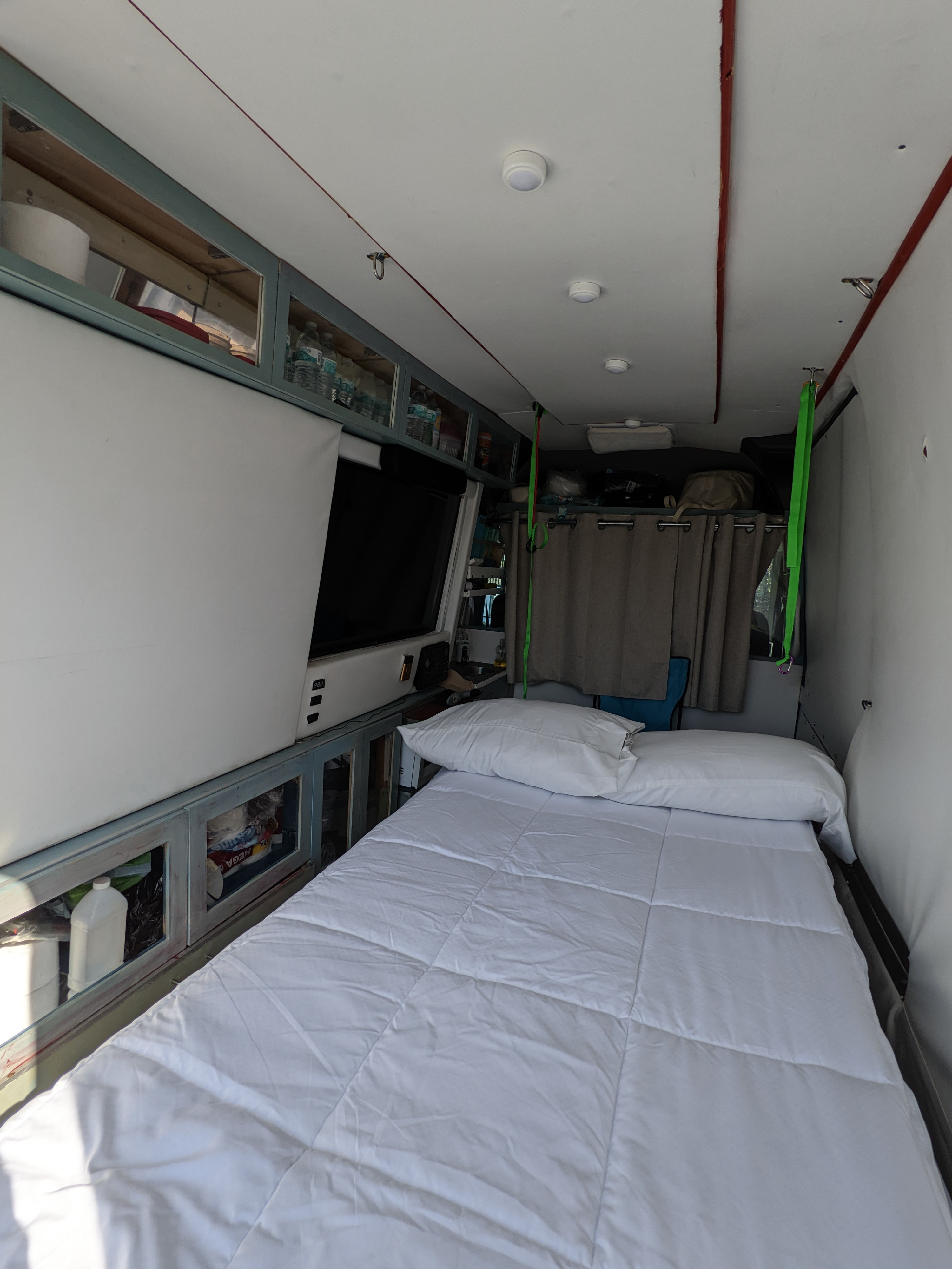 Cozy RV rental interior with a neatly made bed, white bedding, overhead storage cabinets, and a TV/screen setup.. Mercedes Benz Sprinter 2500 144 2007