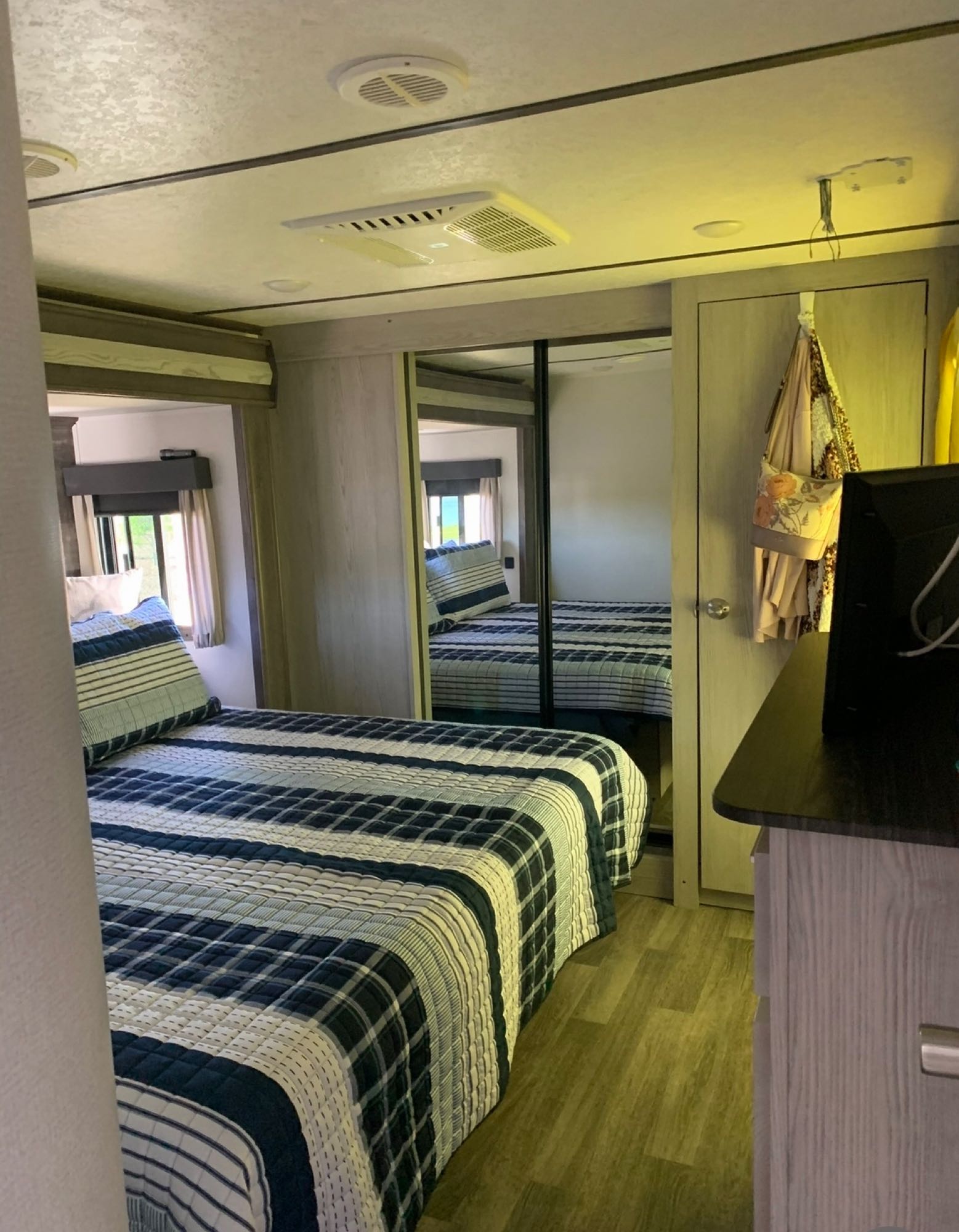 Cozy RV rental bedroom with a striped bedspread, mirrored closet, and window, perfect for your next adventure.. Keystone RV Montana High Country 2020