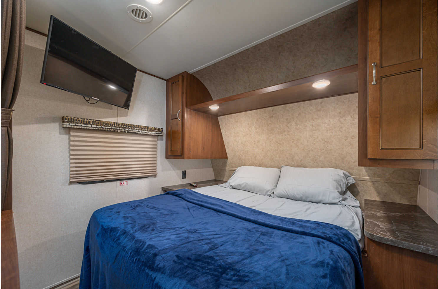 Comfy RV rental bedroom with a bed, mounted TV, wooden overhead cabinets, and window blinds.. Jayco Jay Flight 2017