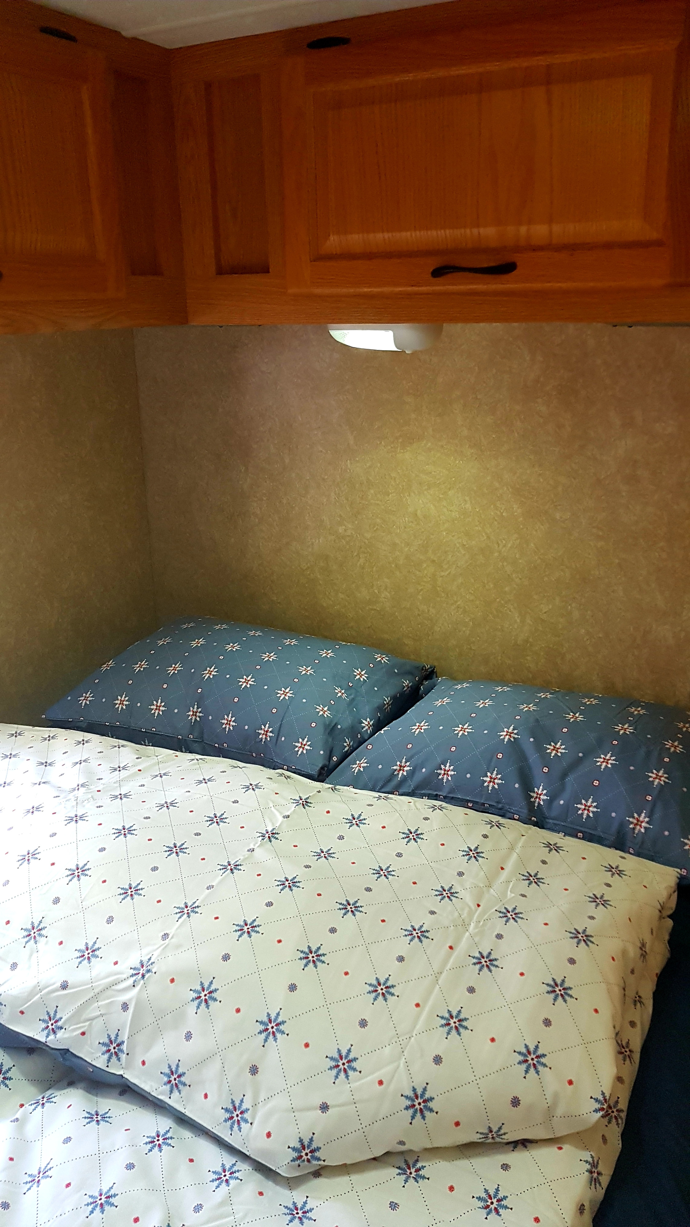 Comfortable sleeping area in an RV rental, featuring snowflake-patterned bedding under wooden cabinets and a task light.. Thor Majestic 2010