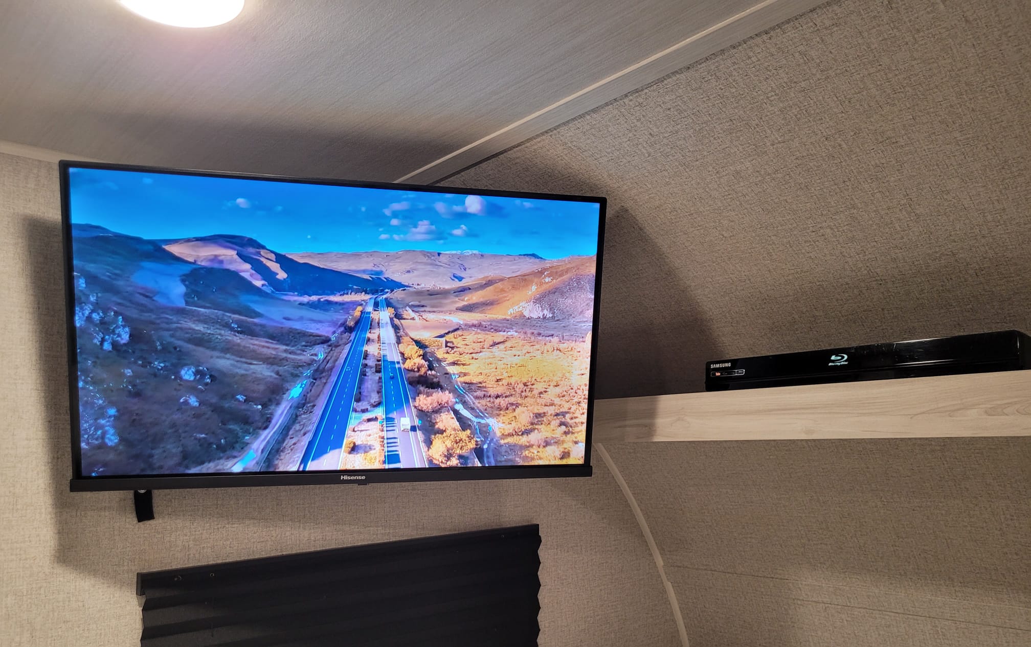 An RV rental interior features a Hisense TV showing a highway scene and a Samsung Blu-ray player on a shelf.. East to West Della Terra 2023