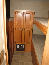 This RV rental bunkhouse features wooden bunk beds, a central wardrobe, and additional storage cabinets, all on a tiled floor.. Forest River Palomino Puma 2010