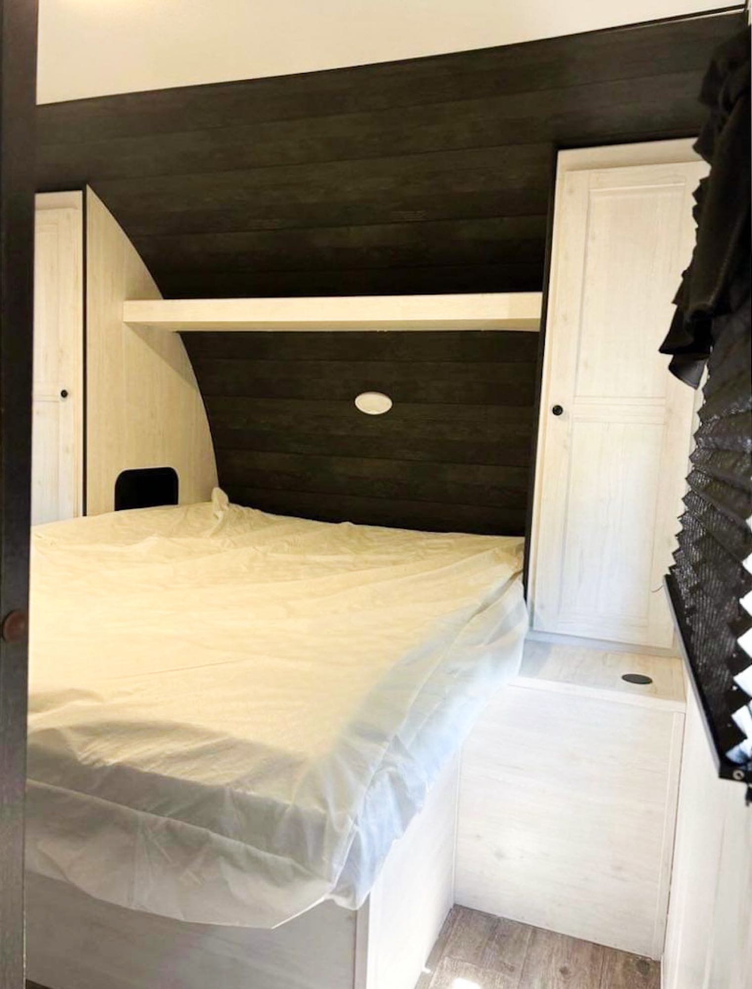 RV rental bedroom showcasing a white bed, dark wood headboard, and light wood cabinetry with shelf.. Heartland RVs Trail Runner 2022