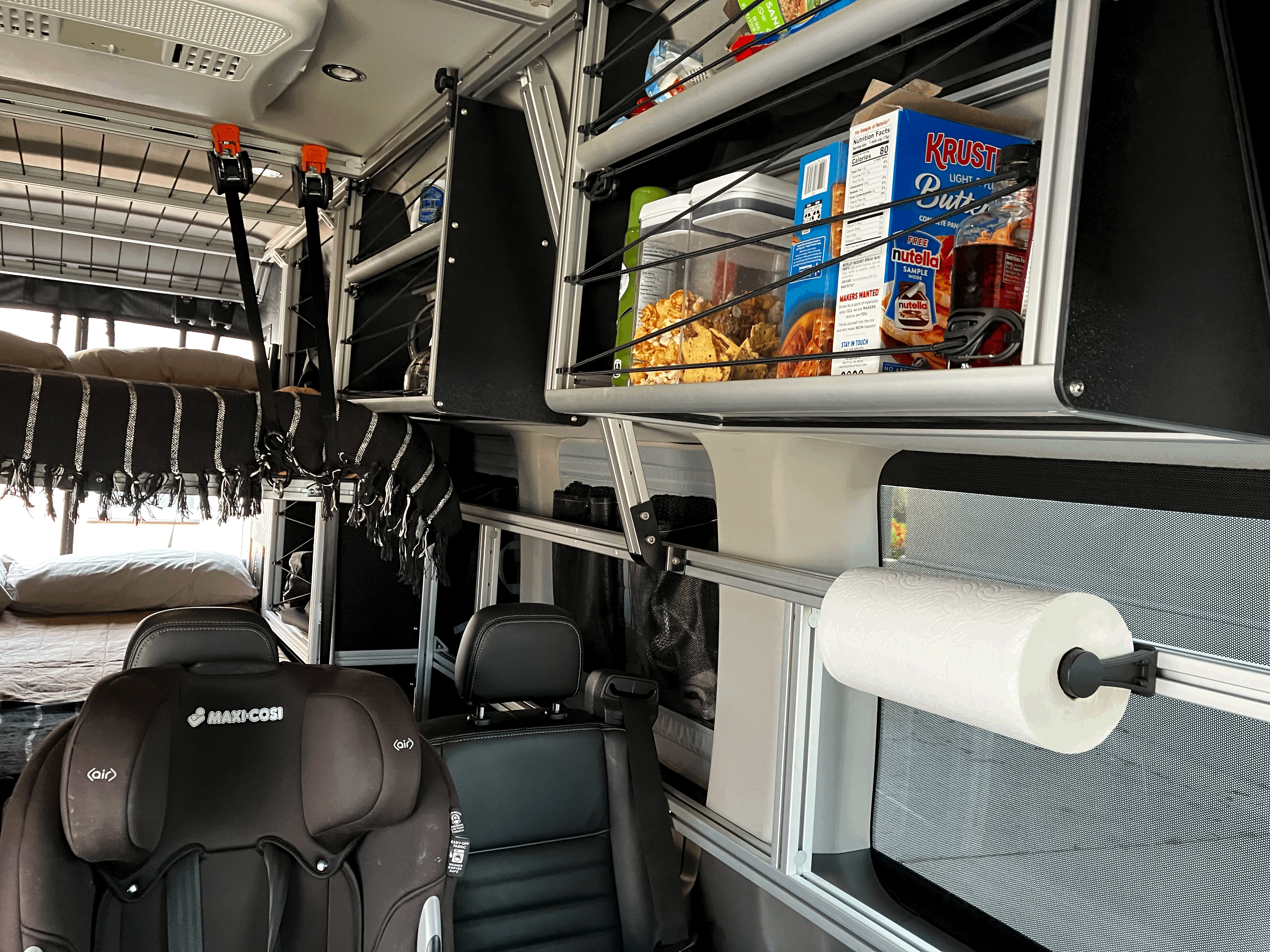 RV rental interior: bunk beds, child car seat, overhead shelving with groceries, and a paper towel holder. Designed for family travel.. Ford Transit Custom 2022