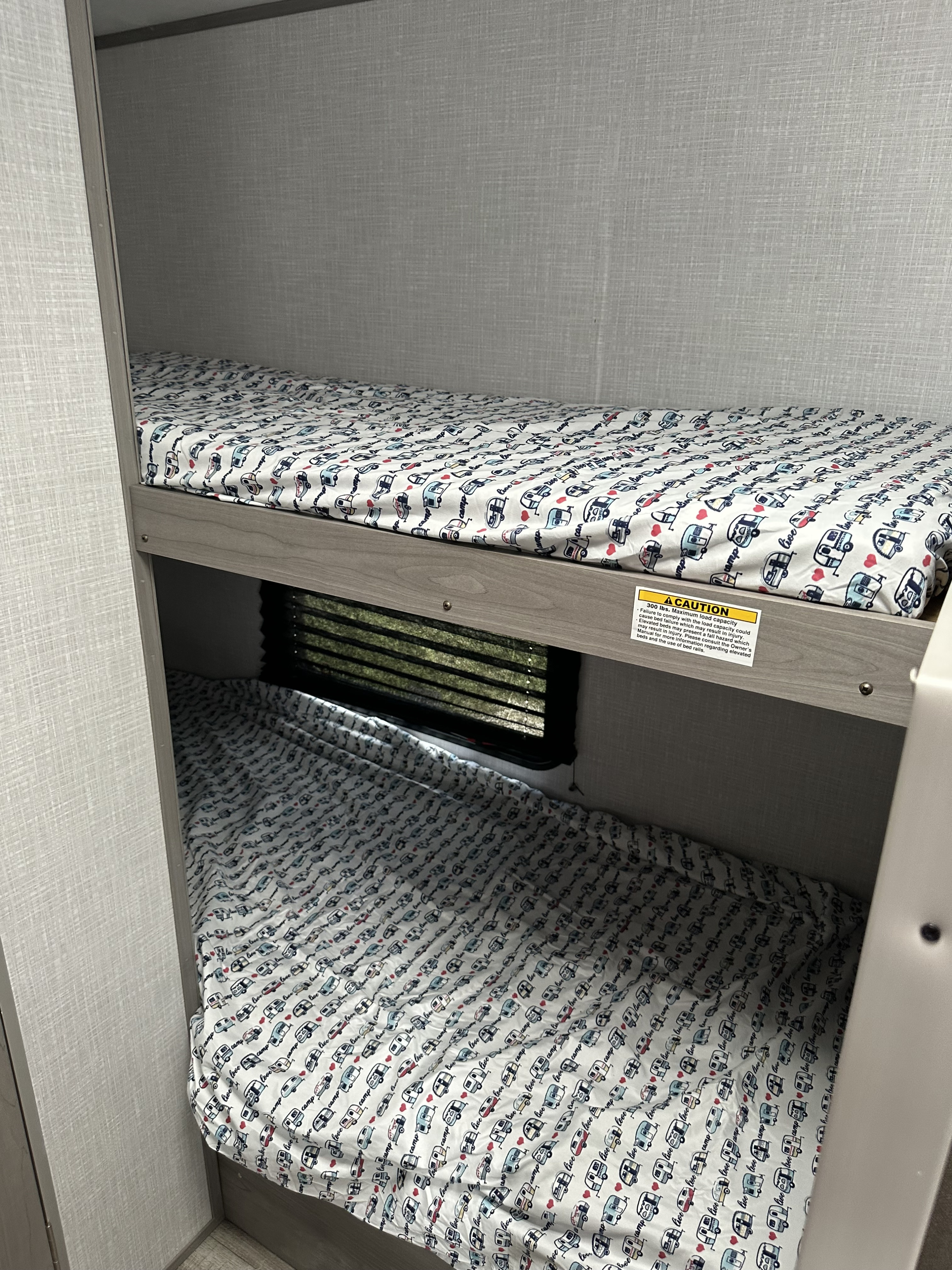 RV rental interior: bunk beds with playful camping sheets, a lower window, and a safety caution label on the upper bunk.. Dutchmen Coleman Lantern LT 2022