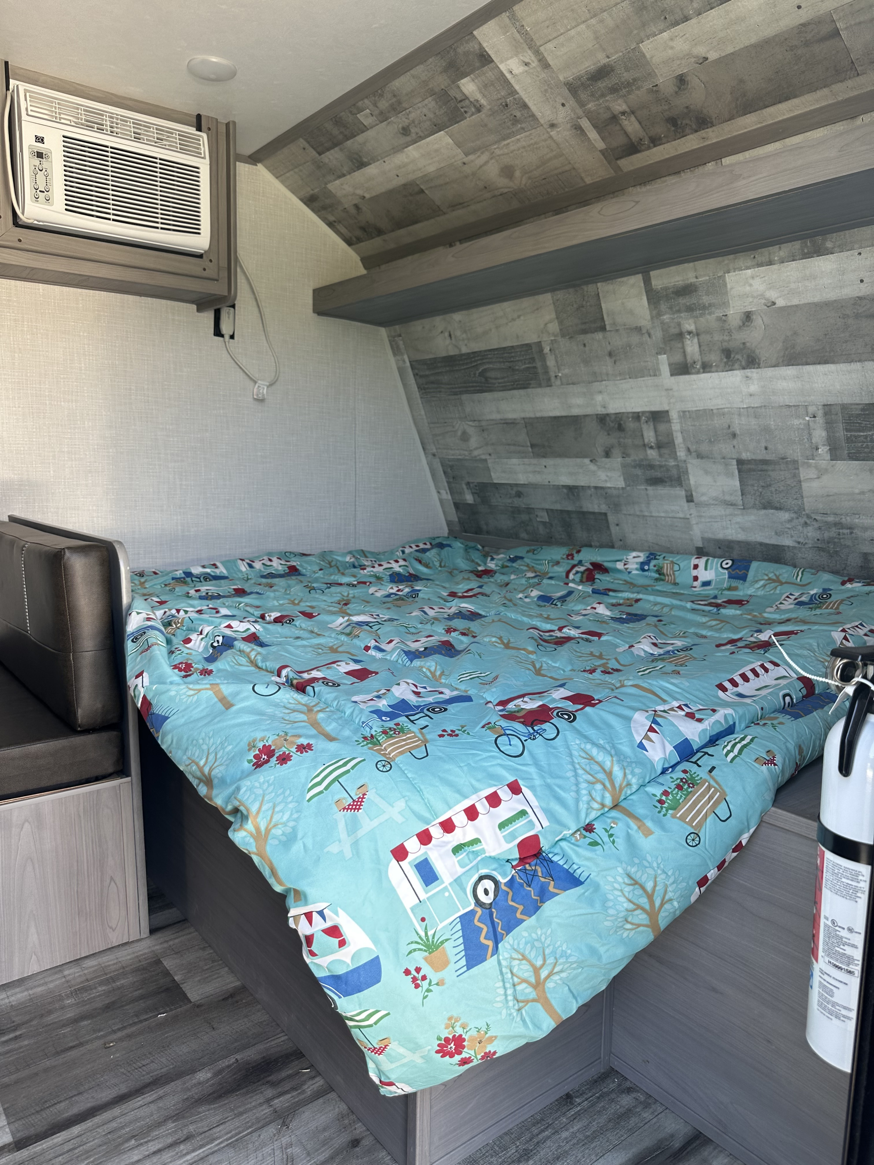 Inside an RV rental: a comfy bed with playful comforter, AC unit, and practical fire extinguisher.. Dutchmen Coleman Lantern LT 2022