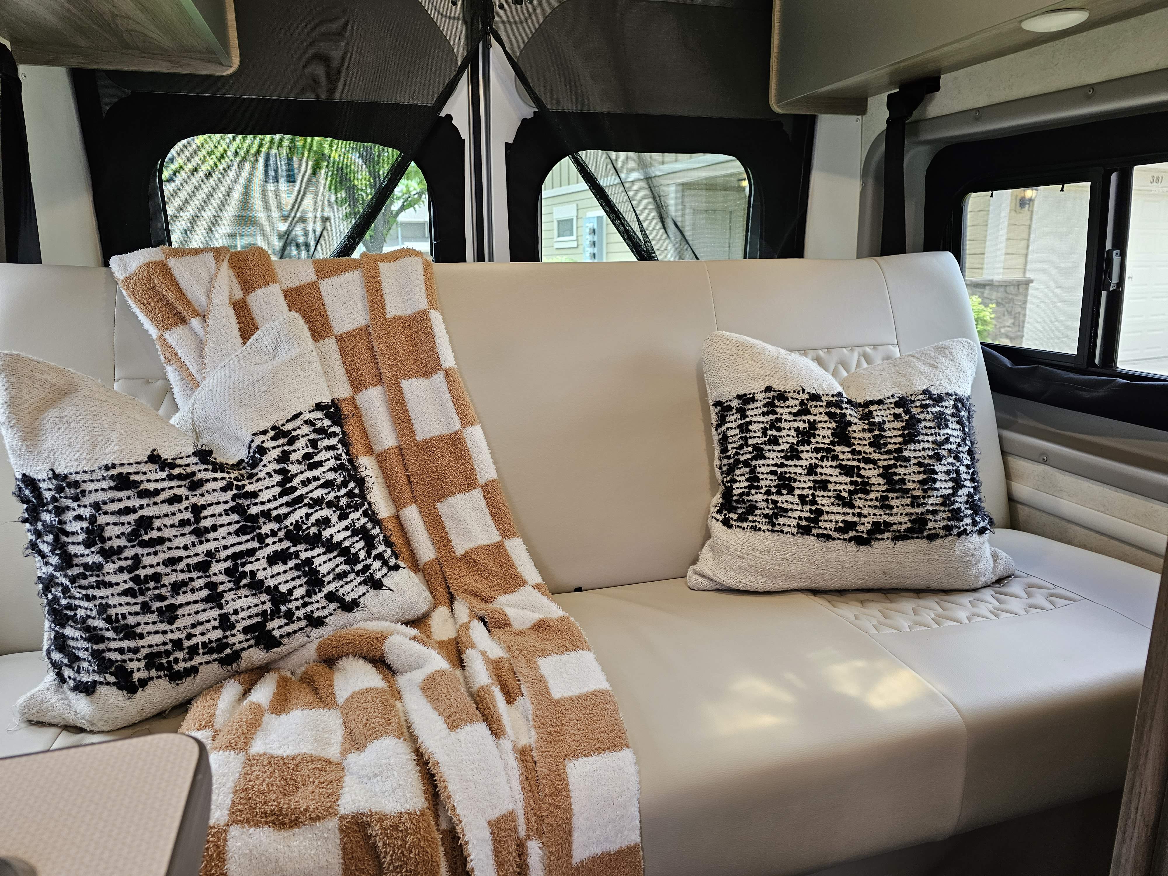 Cozy RV rental interior features light seating, checkered blanket, and textured pillows.. Winnebago Solis 2022