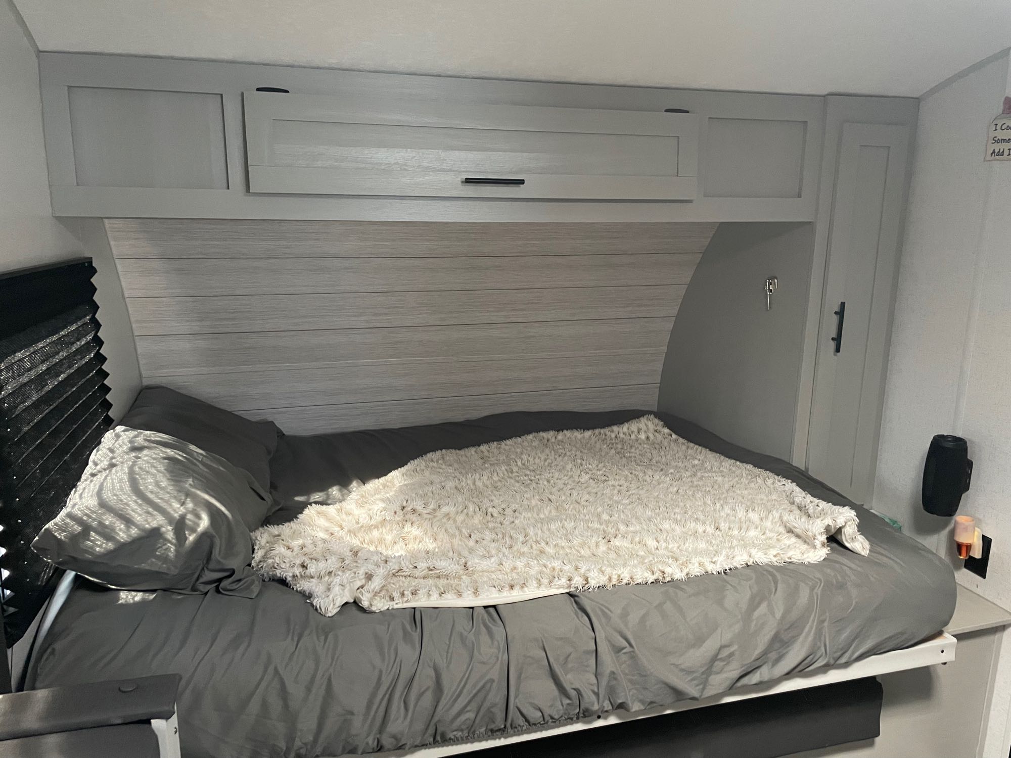 Relaxing RV rental bedroom showing a bed with grey sheets, white fluffy blanket, and light wood cabinetry.. Forest River Wildwood 178 BHSKX 2022