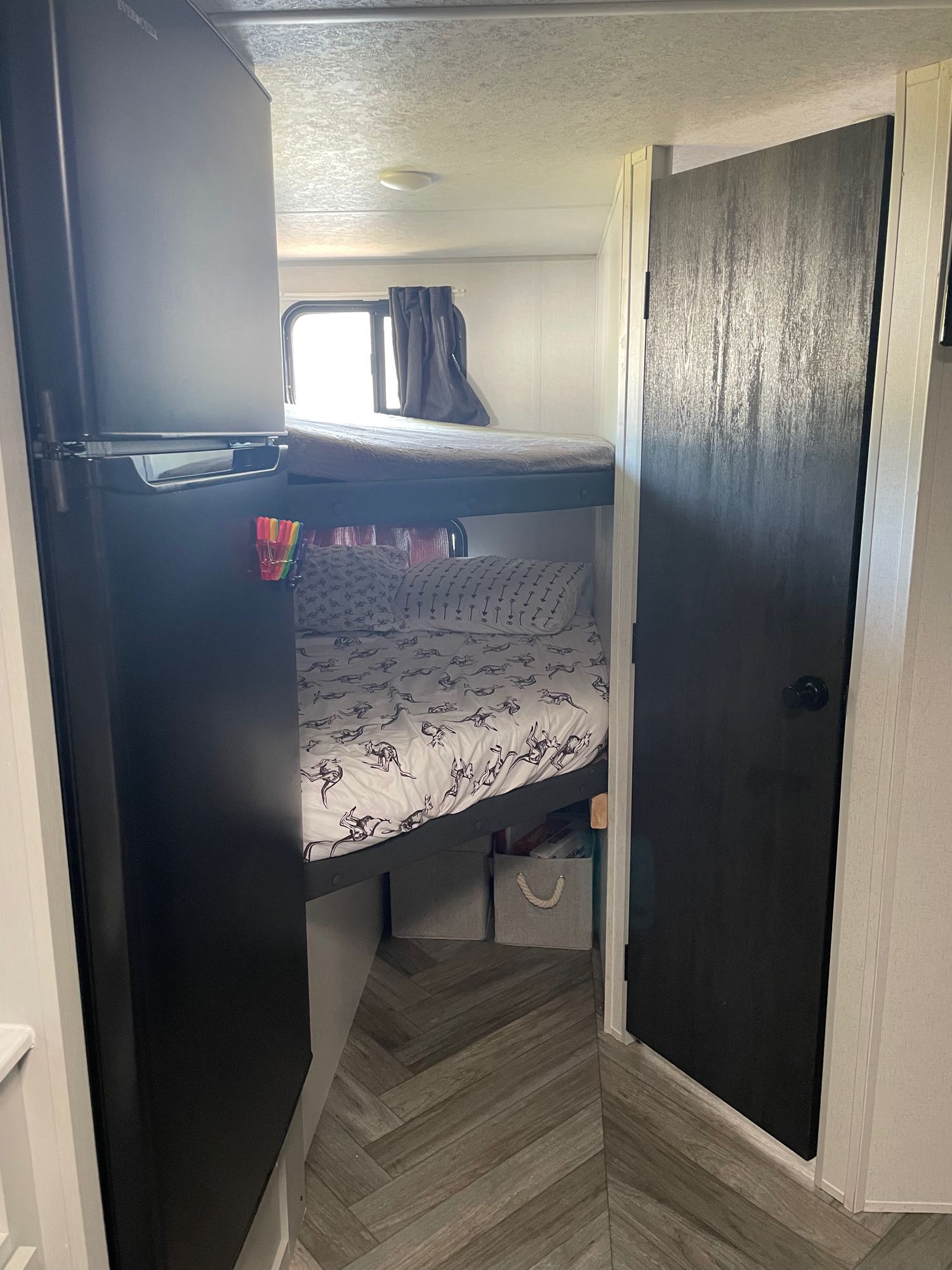 RV rental interior showcasing cozy bunk beds with themed sheets, a small fridge, and a dark open door.. Forest River Wildwood 178 BHSKX 2022