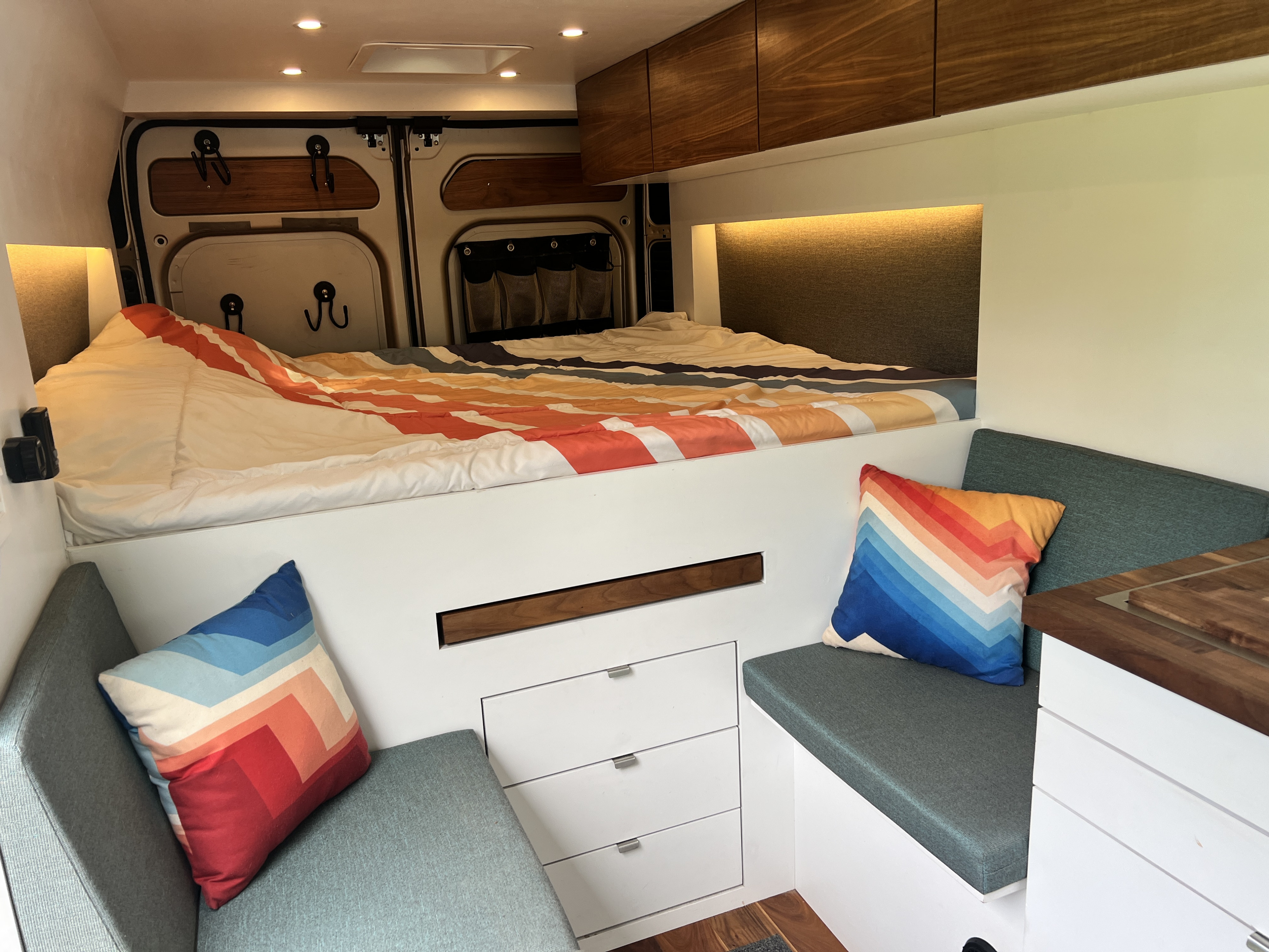 This RV rental interior features a cozy raised bed with bright bedding, comfortable bench seating, and clever storage solutions.. Dodge Ram Promaster 2500 2021