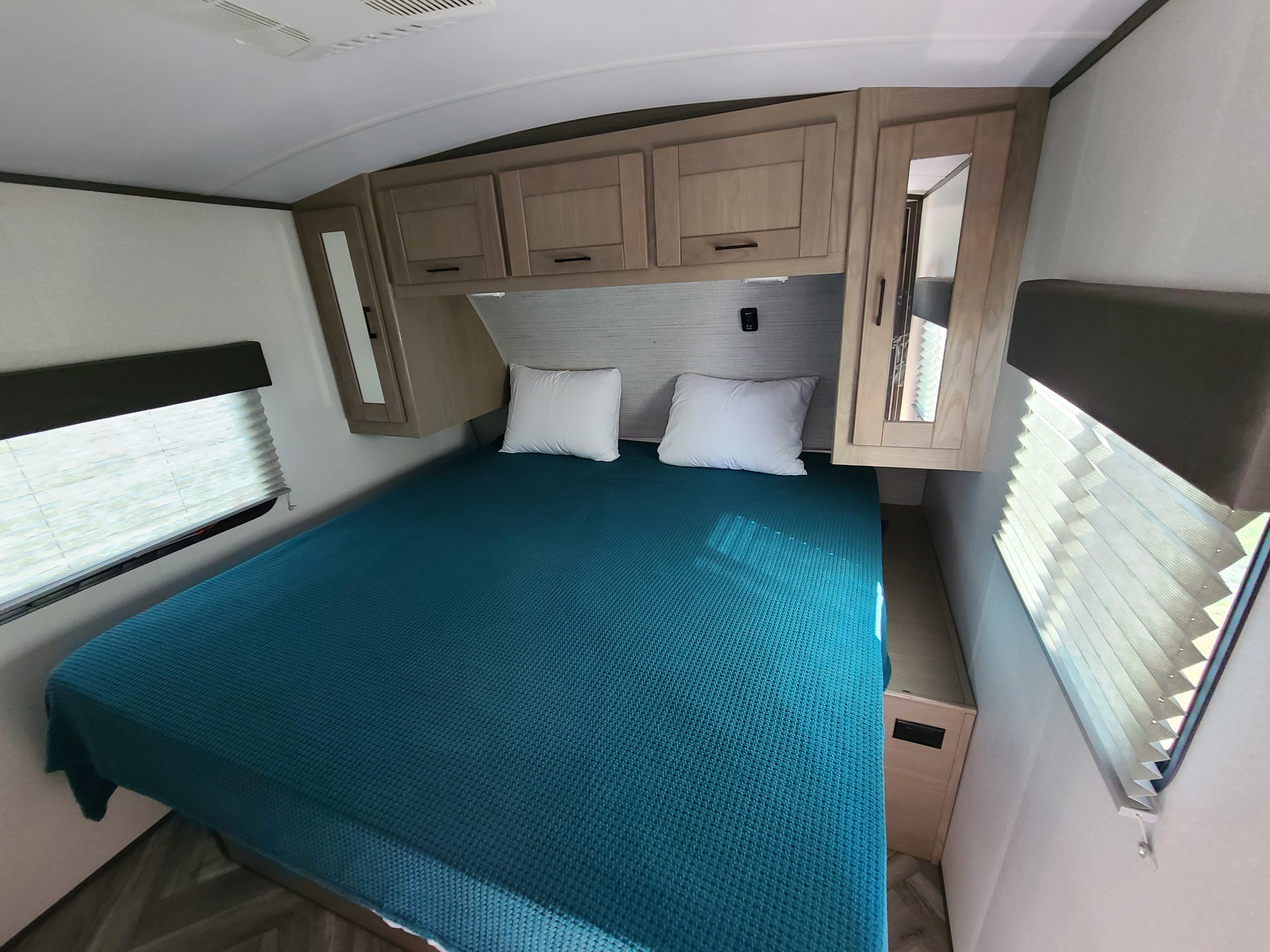 Cozy RV rental bedroom with a bed, teal cover, overhead cabinets, window blinds, and ceiling vent.. Cruiser Rv Corp Shadow Cruiser 2020