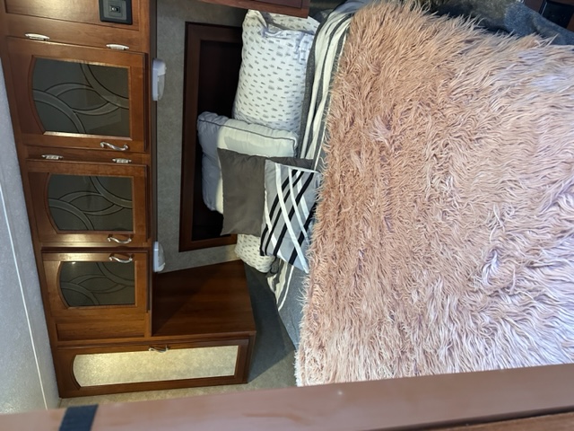 Cozy RV rental bedroom featuring fluffy pink bedding and built-in wooden cabinets with patterned glass inserts.. Forest River Tracer Ultra Lite Executive 2014