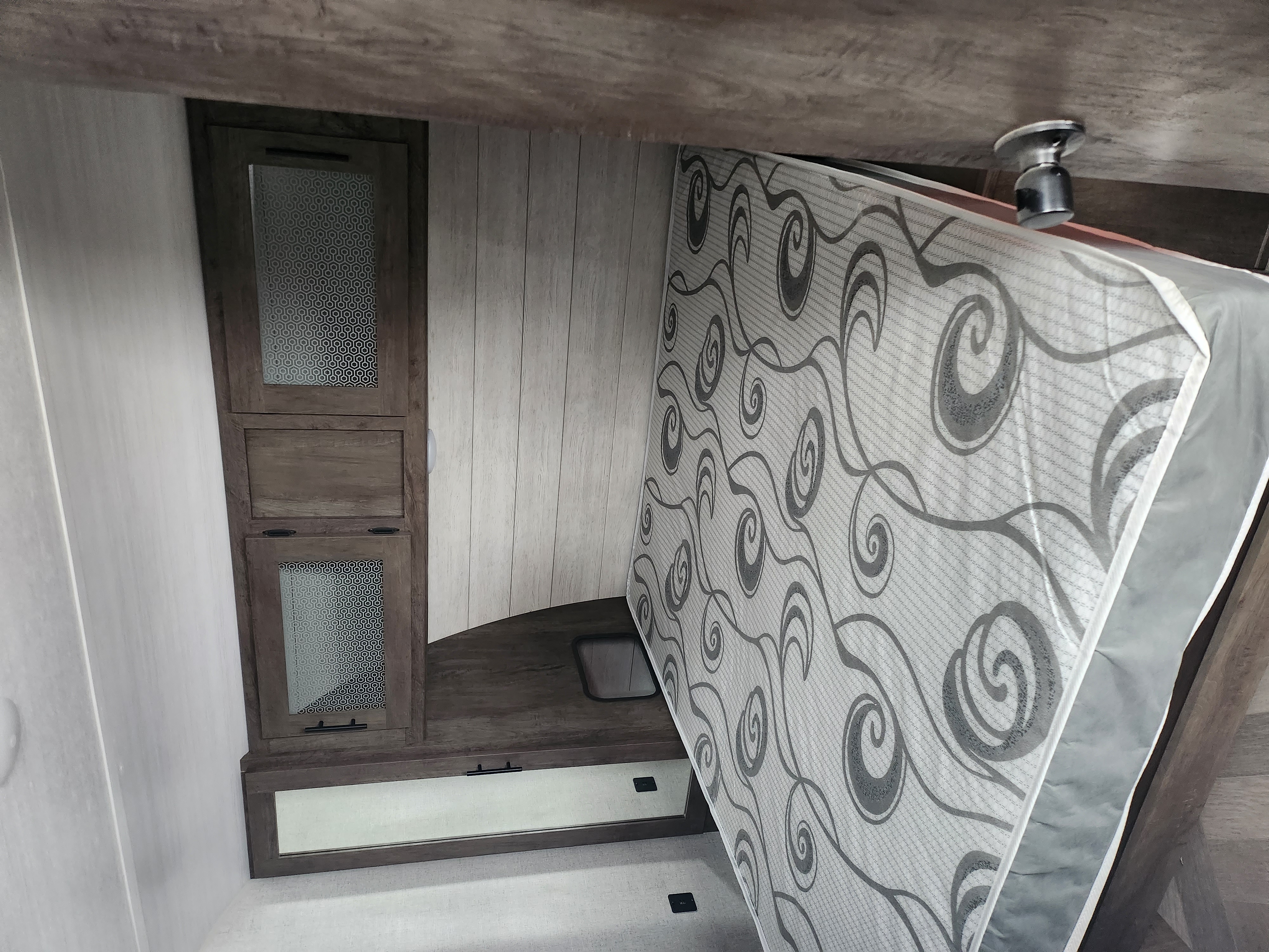 RV rental interior: A lifted mattress reveals under-bed storage next to wood cabinets with patterned glass panels.. Forest River Salem 2020