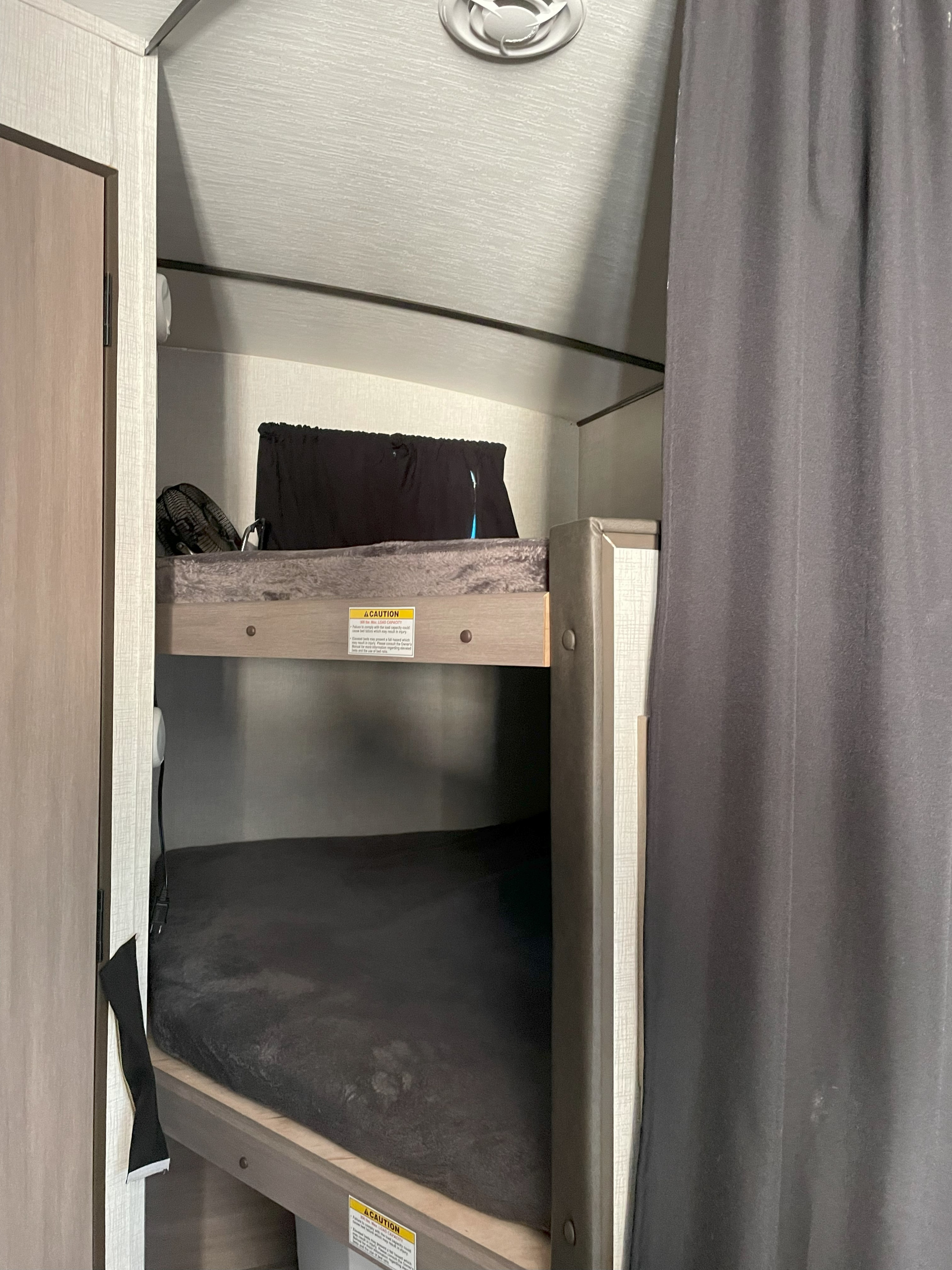 Inside an rv rental, showcasing compact bunk beds with dark bedding, providing cozy sleeping quarters for trips.. Sunset Park RV 272BH 2022