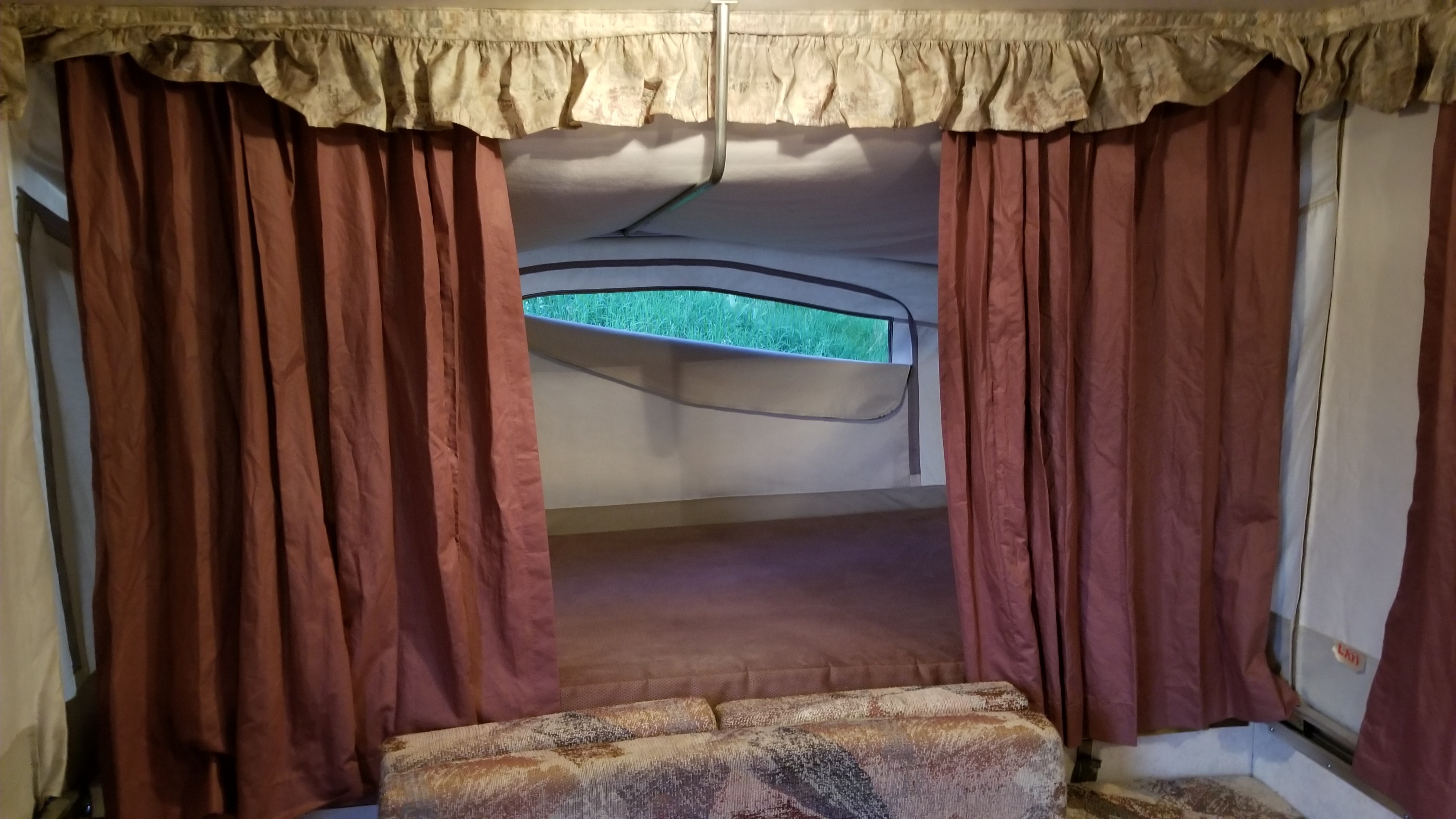 RV rental interior: opened brown curtains reveal a sleeping bunk and window looking out to green grass.. Damon Outlaw 1996