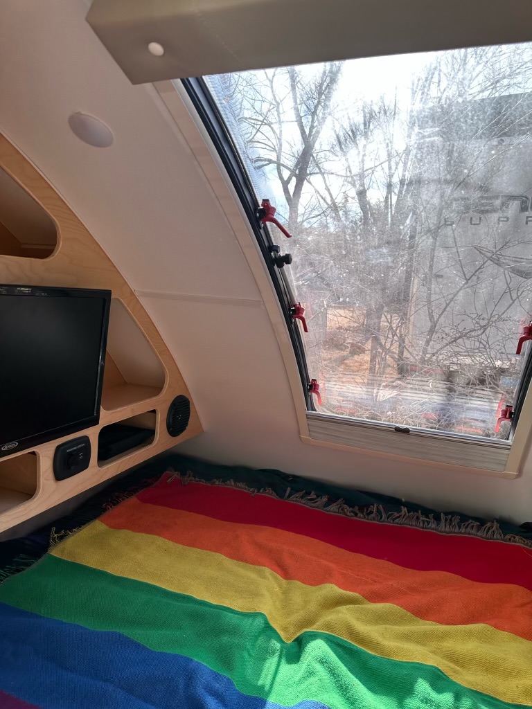 Teardrop RV rental interior: Cozy bed with a rainbow blanket, TV, and large window view.. Little Guy Little Guy Trailer 2020
