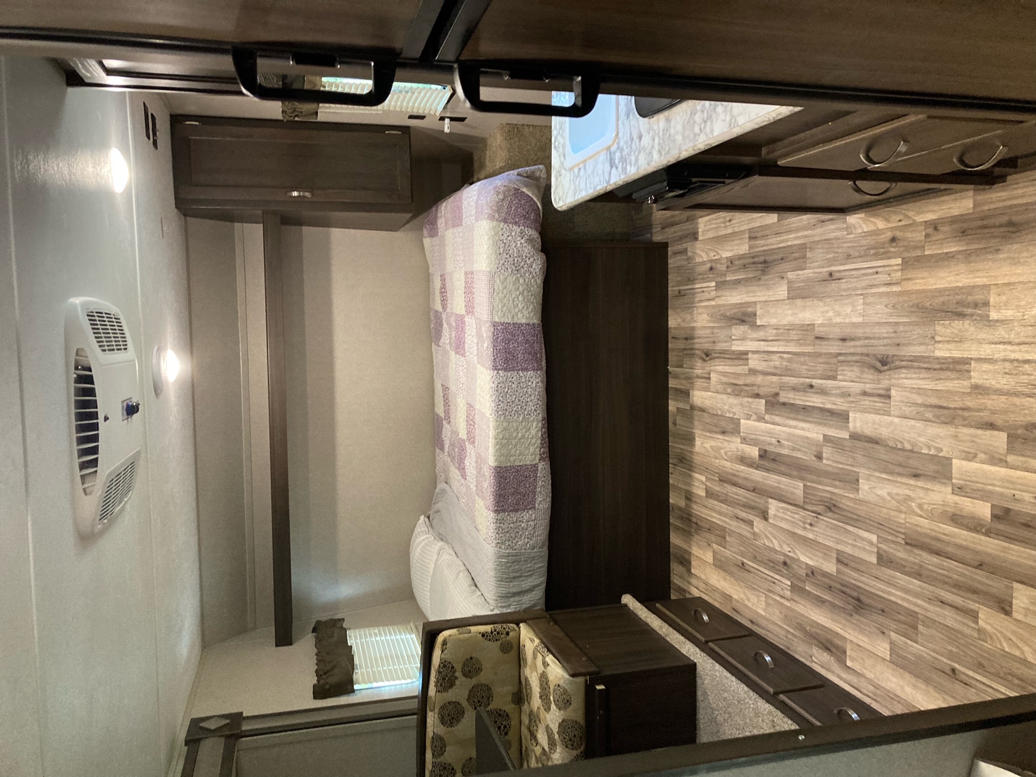 Interior view of an RV rental showing a compact bedroom with a purple quilt, a kitchen counter, and a small seating area.. Keystone RV Springdale 2019