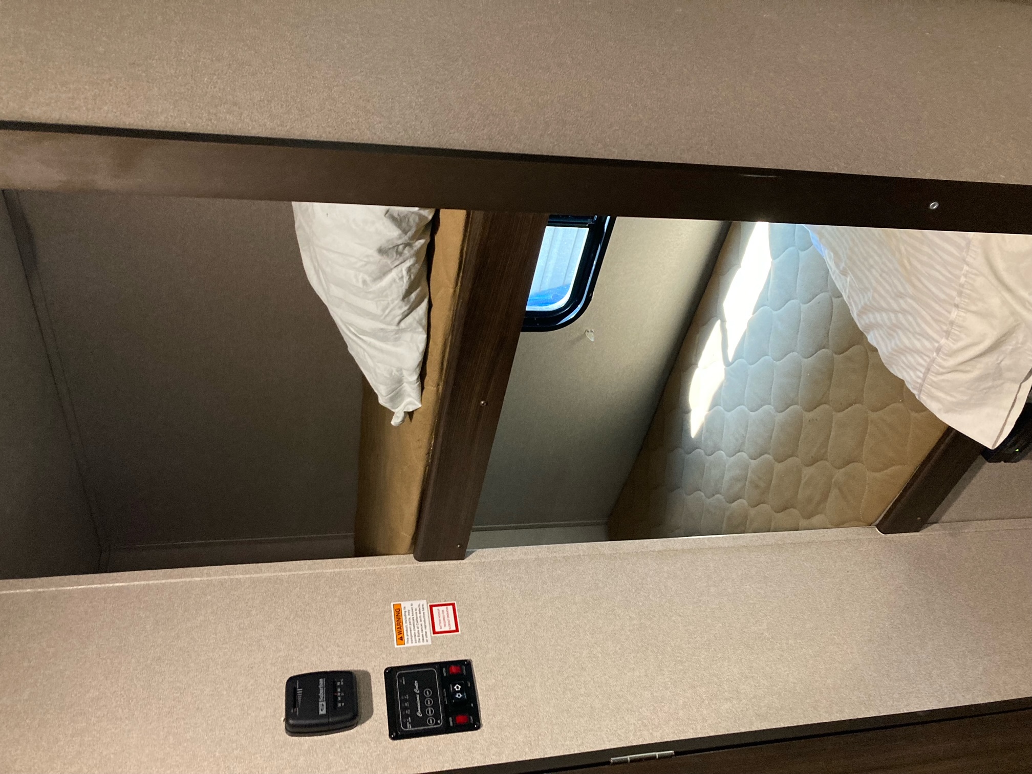 Cozy RV rental bunk beds seen from below. Features include a window, bedding, and a control panel for RV functions.. Keystone RV Springdale 2019