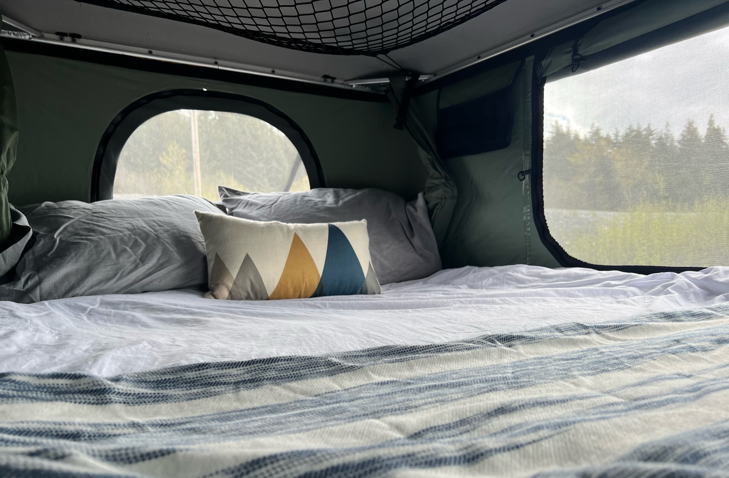 Relax in this RV rental! A cozy bed with fresh linens & mountain pillow offers views through mesh windows to the trees.. Toyota Tacoma 2012