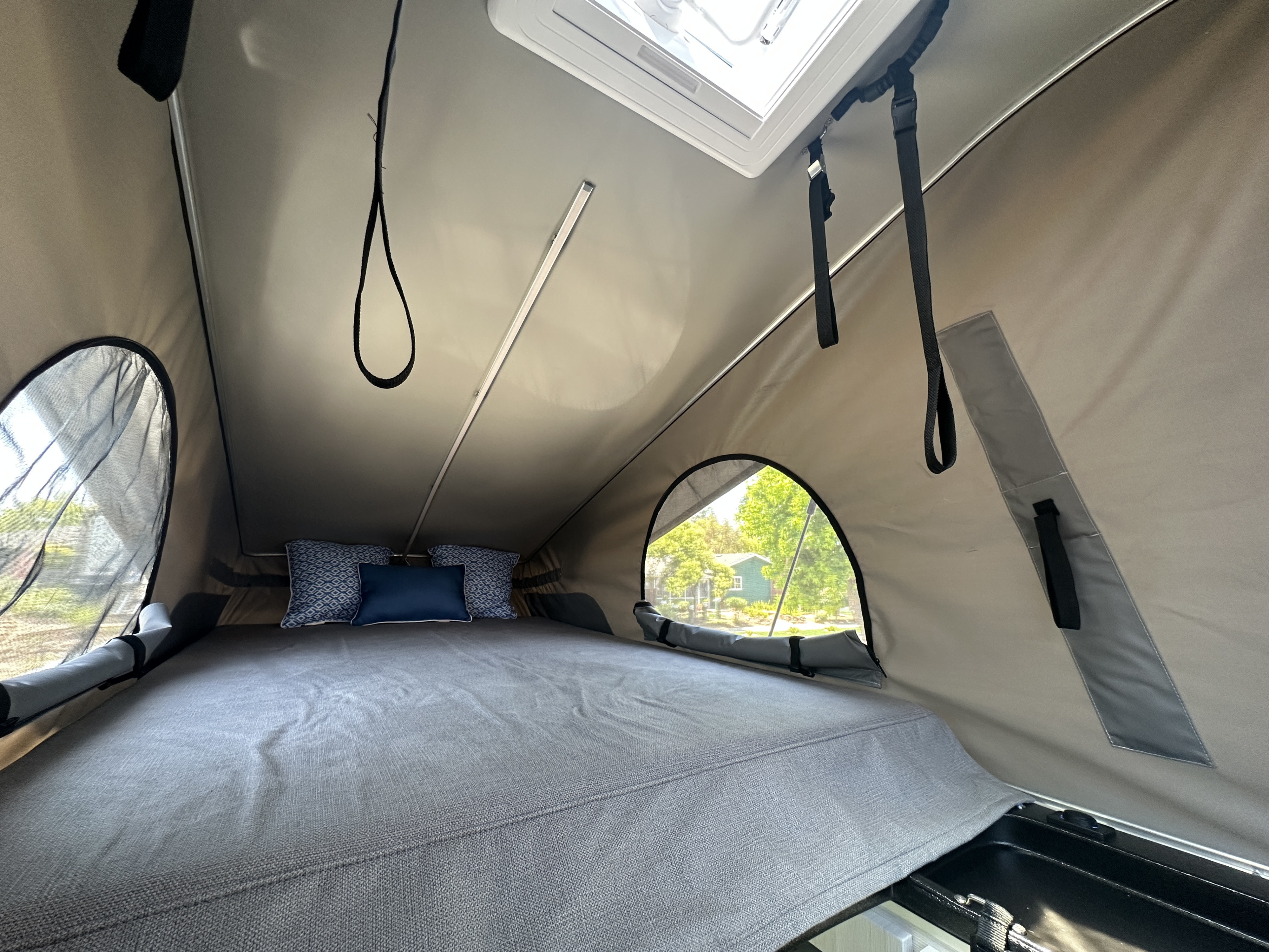 Comfortable pop-top RV rental sleeping area with a gray bed, blue pillows, and screened windows offering natural views.. Dodge Ram ProMaster RoadTrek Zion Slumber 2023