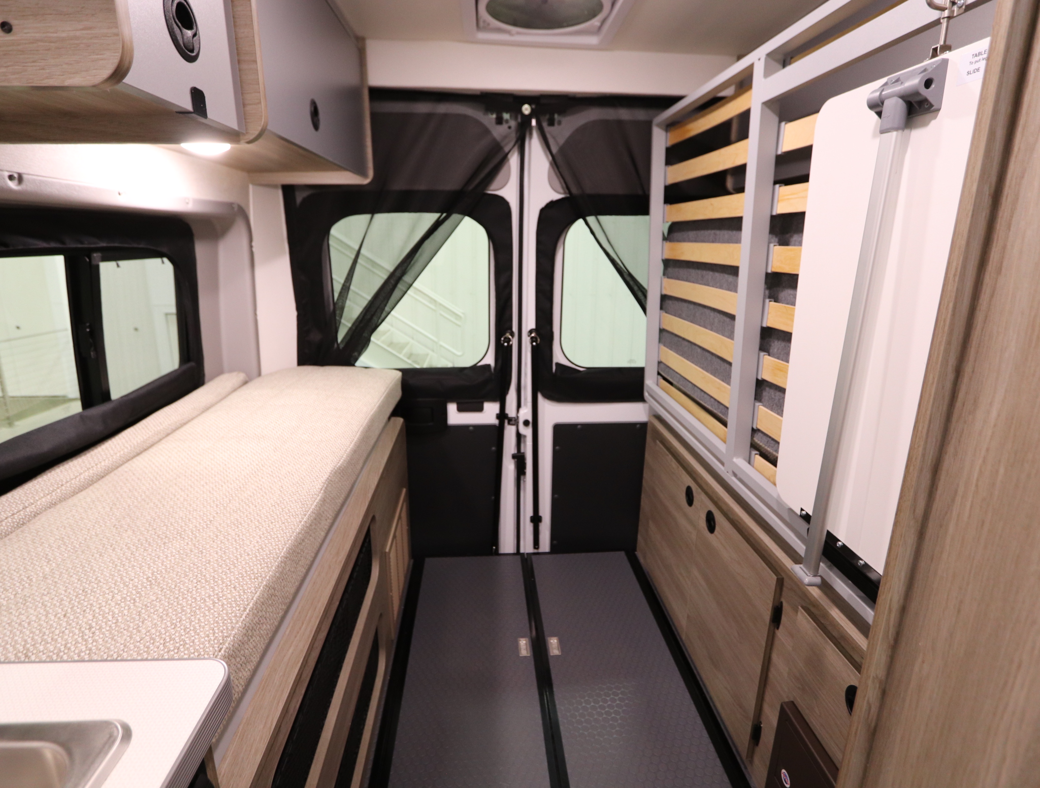 Inside a modern RV rental: a compact interior with bed, overhead storage, rear doors with mesh, and a multi-functional table/bed setup.. Winnebago Solis 2021