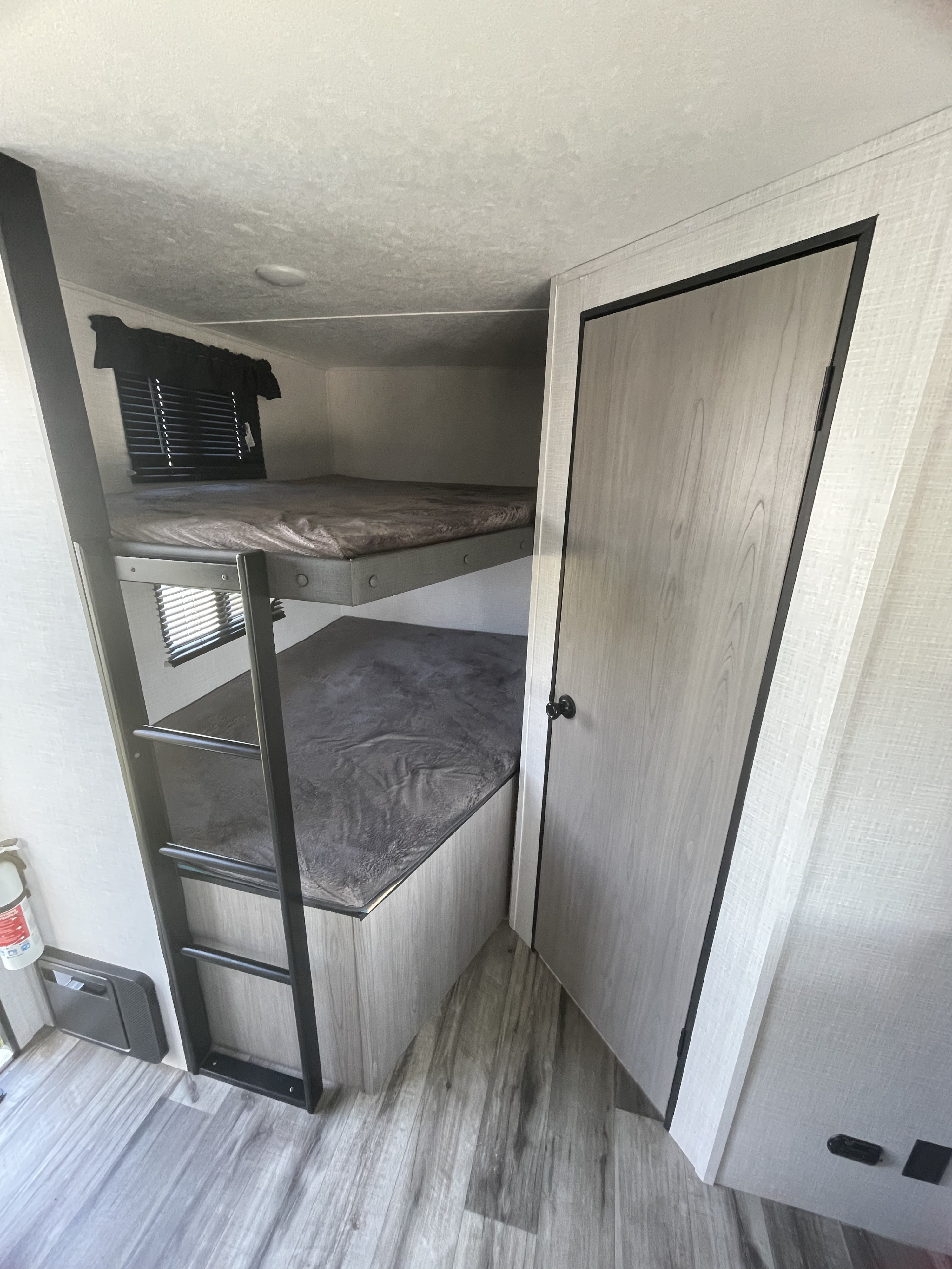 Inside this RV rental: modern bunk beds with a ladder provide comfortable sleeping. A door is on the right.. Dutchmen Coleman Light 2022