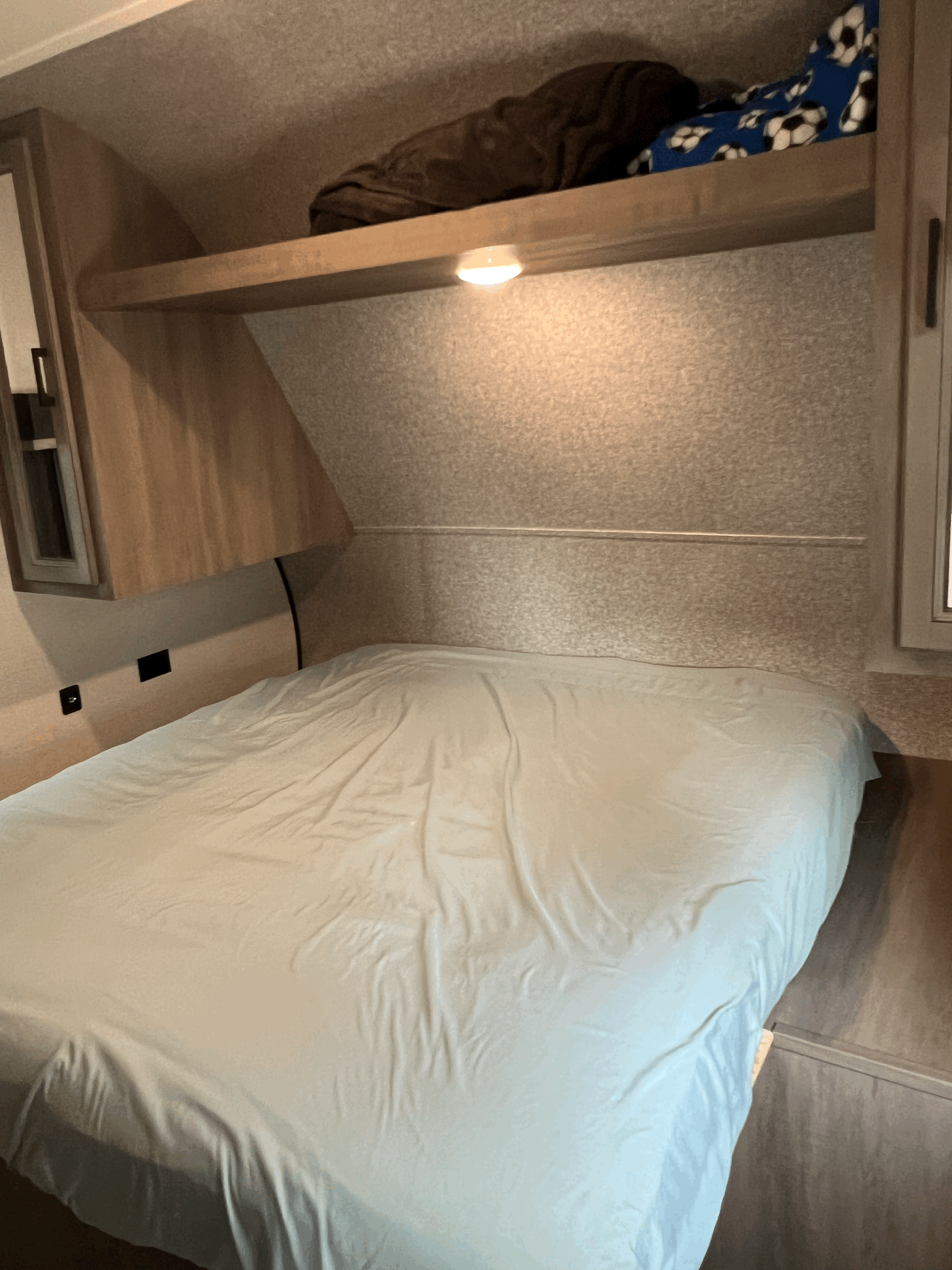 This RV rental bedroom features a comfy bed, an overhead shelf with a reading light, and wall outlets.. Highland Ridge RV Open Range 2022