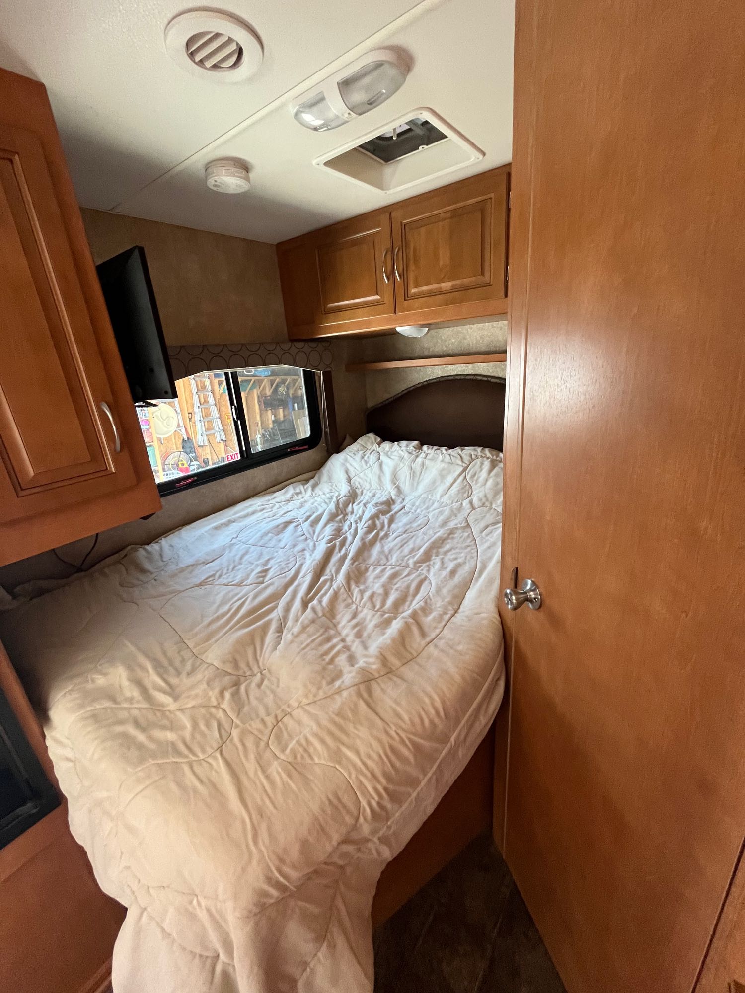 Cozy RV rental interior bedroom with queen bed, wood cabinets, and window. Ideal for comfortable travel.. Winnebago Minnie Winnie 2014