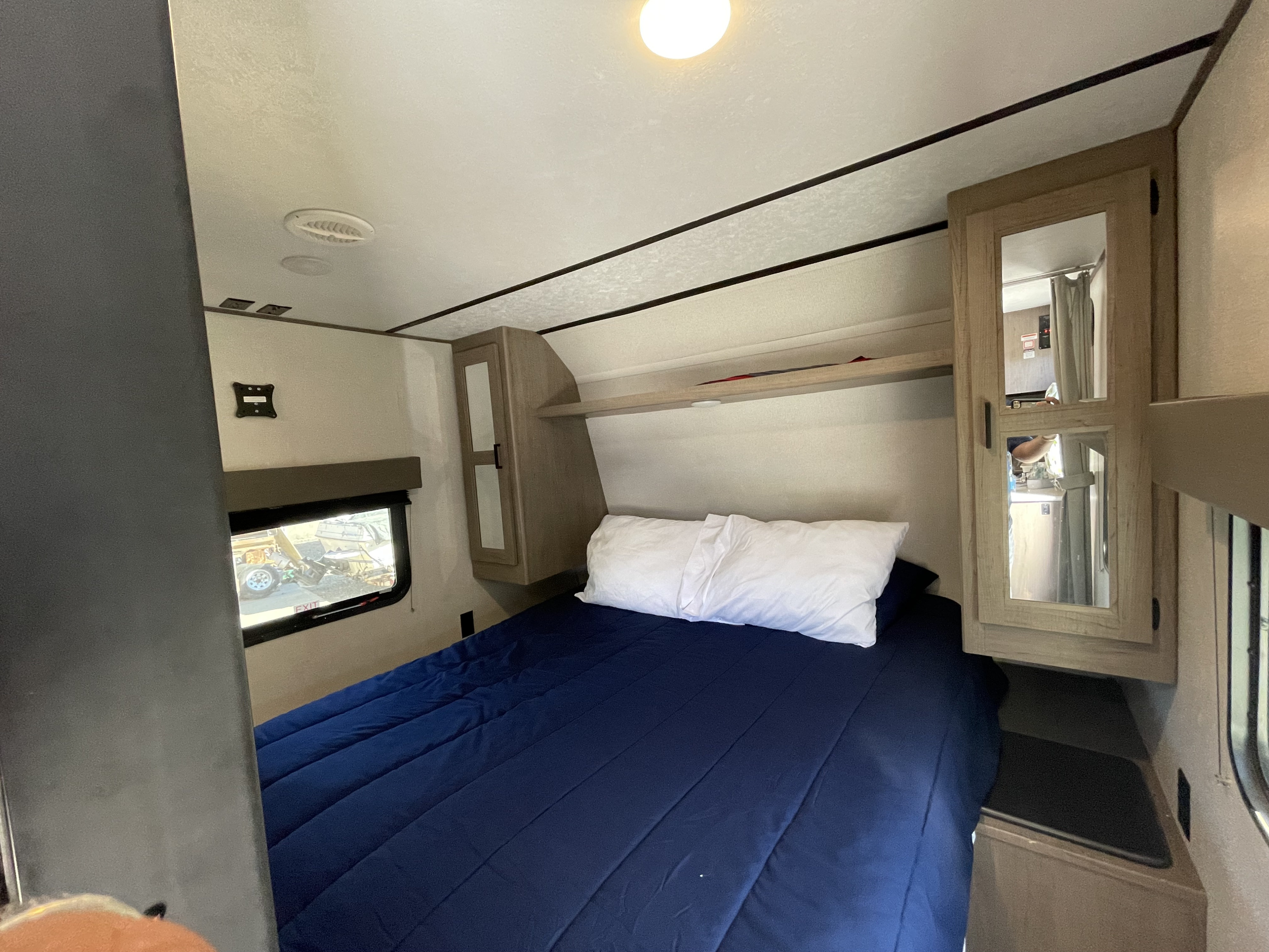 This RV rental offers a compact bedroom with a comfy bed, blue comforter, and overhead storage.. Keystone Hideout 2021