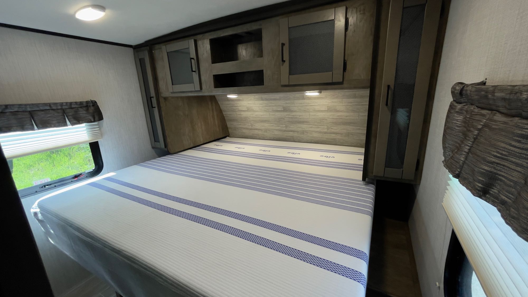 Cozy RV rental bedroom featuring a queen bed with a 'Vibe' mattress, overhead cabinets, and a scenic window view.. Heartland RVs Wilderness 2021
