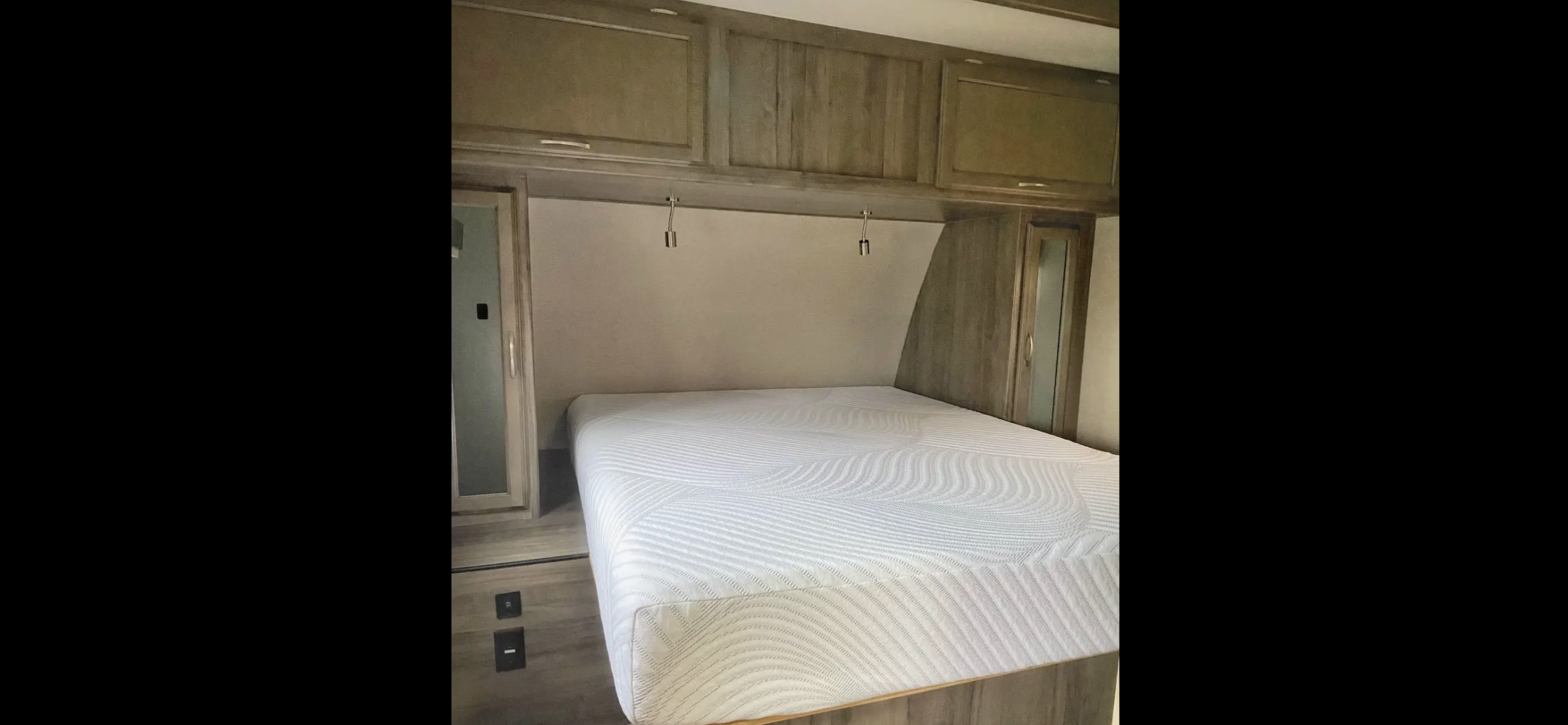 RV rental bedroom: Neutral interior with textured white mattress, overhead and side wood cabinets.. Minnie Minnie Plus 2018